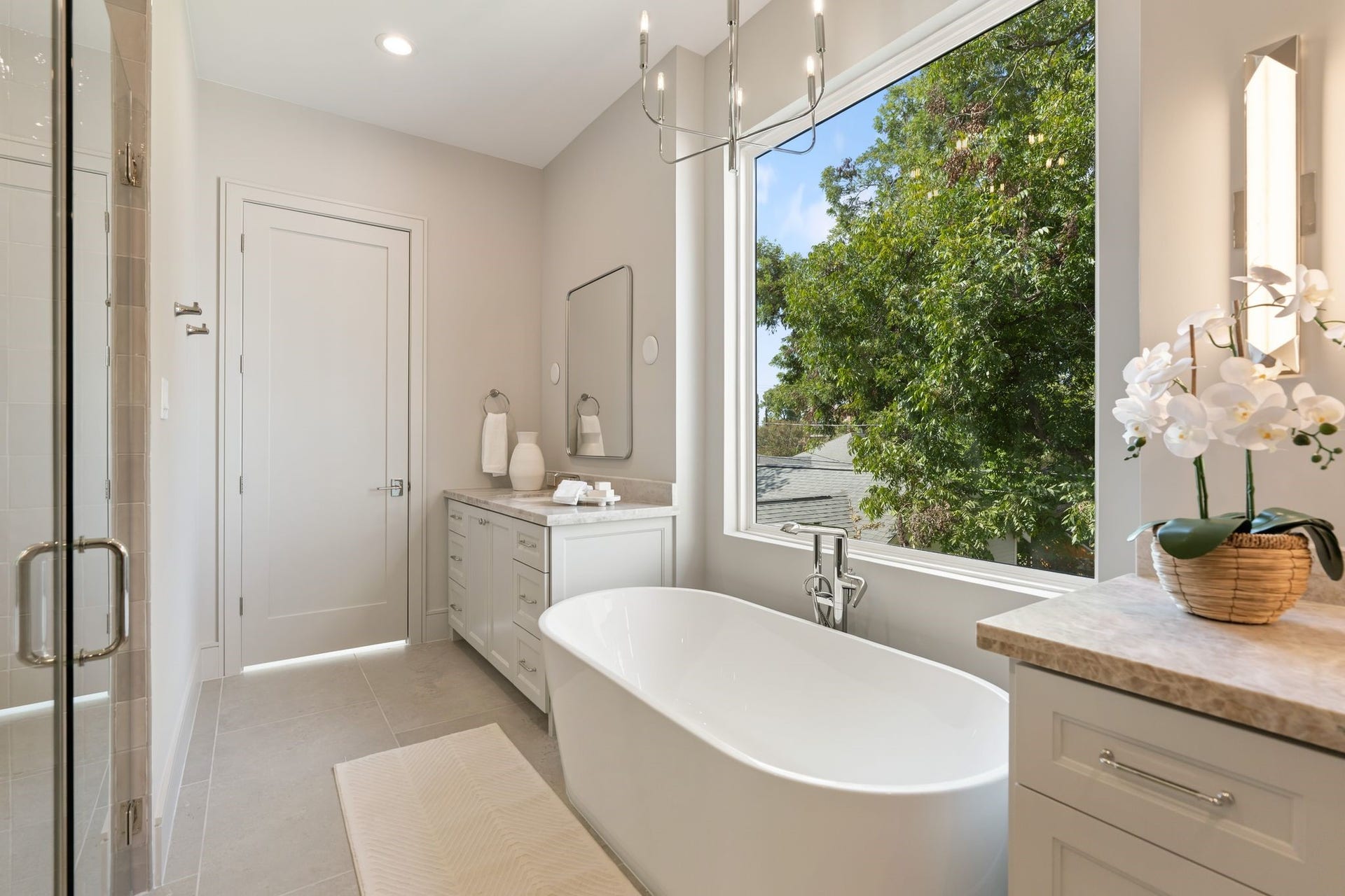 711 E 12th Street, Houston, TX 77008 Soak beneath the treetops in the freestanding Wyndham Carissa tub, positioned beside an expansive window framing leafy views. A Visual Comfort Brianna chandelier adds elegance overhead.