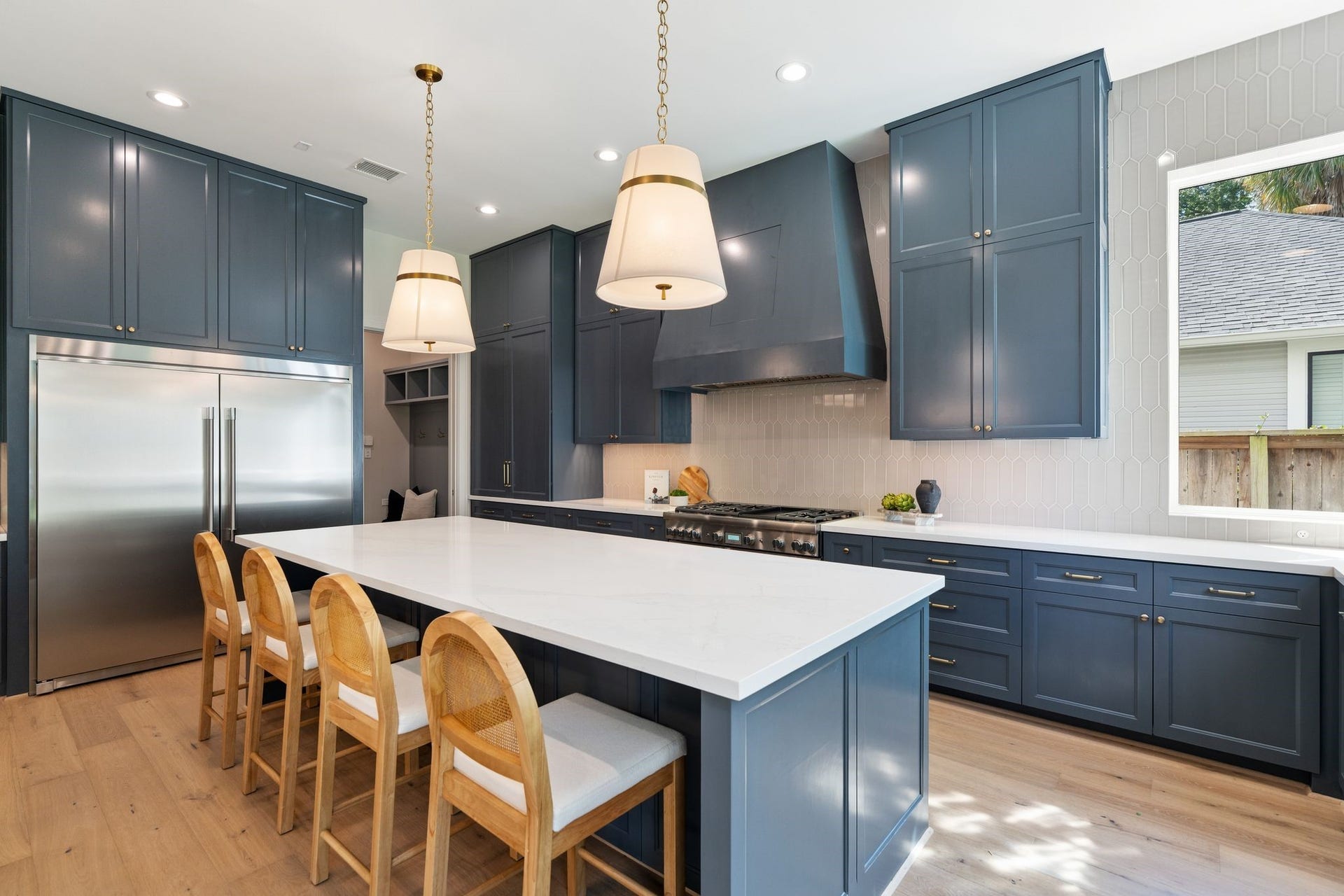 711 E 12th Street, Houston, TX 77008 A generous island with seating for four anchors this beautifully appointed kitchen. Brass pendants and a ceiling-height picket tile backsplash add warmth and texture.