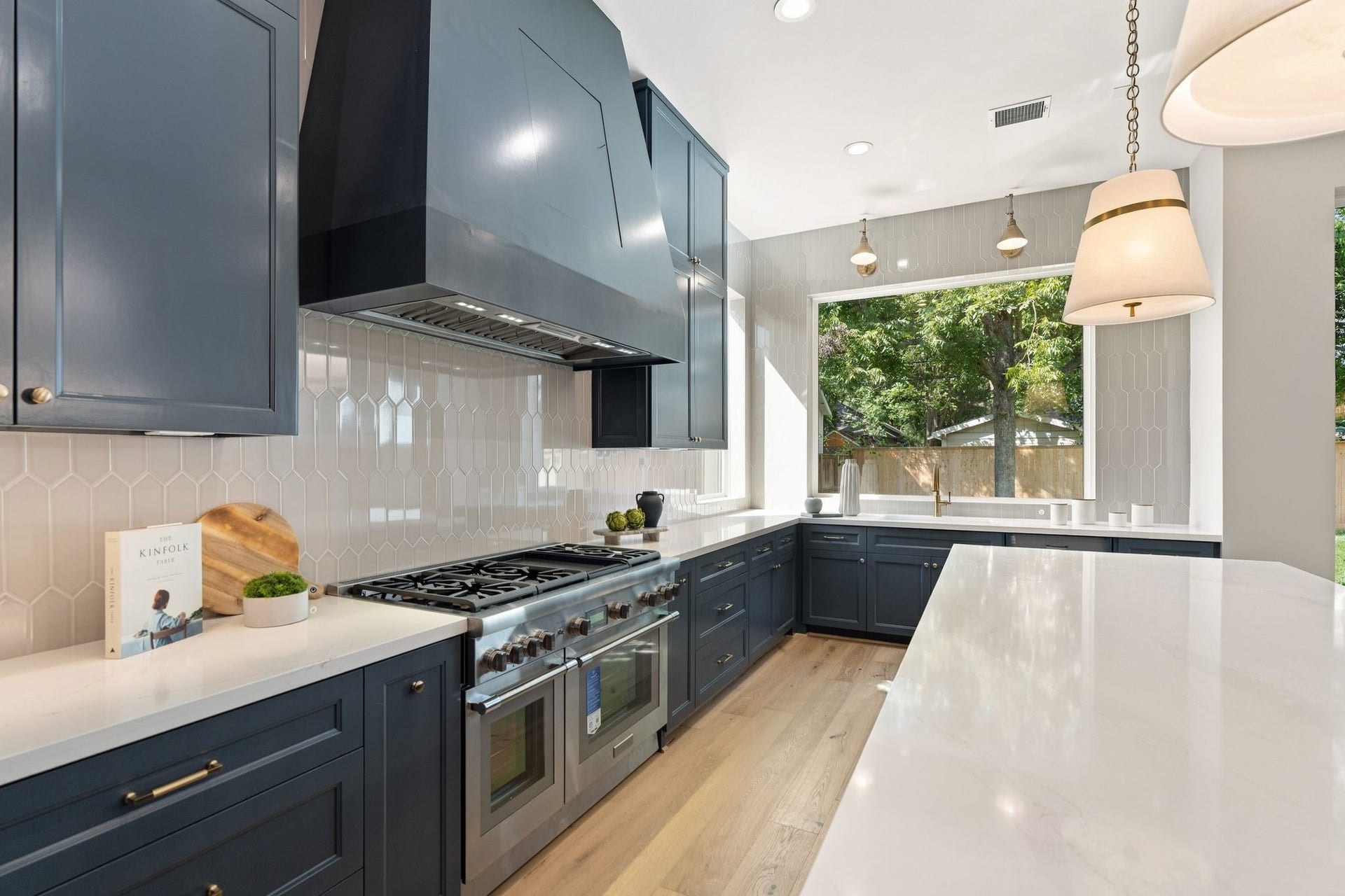 711 E 12th Street, Houston, TX 77008 Custom cabinetry in Sherwin-Williams Outerspace contrasts beautifully with Silestone Ethereal Glow quartz counters and a ceiling-height picket tile backsplash. Brass pendants add warmth, while a 48-inch Thermador range brings serious cooking capability.