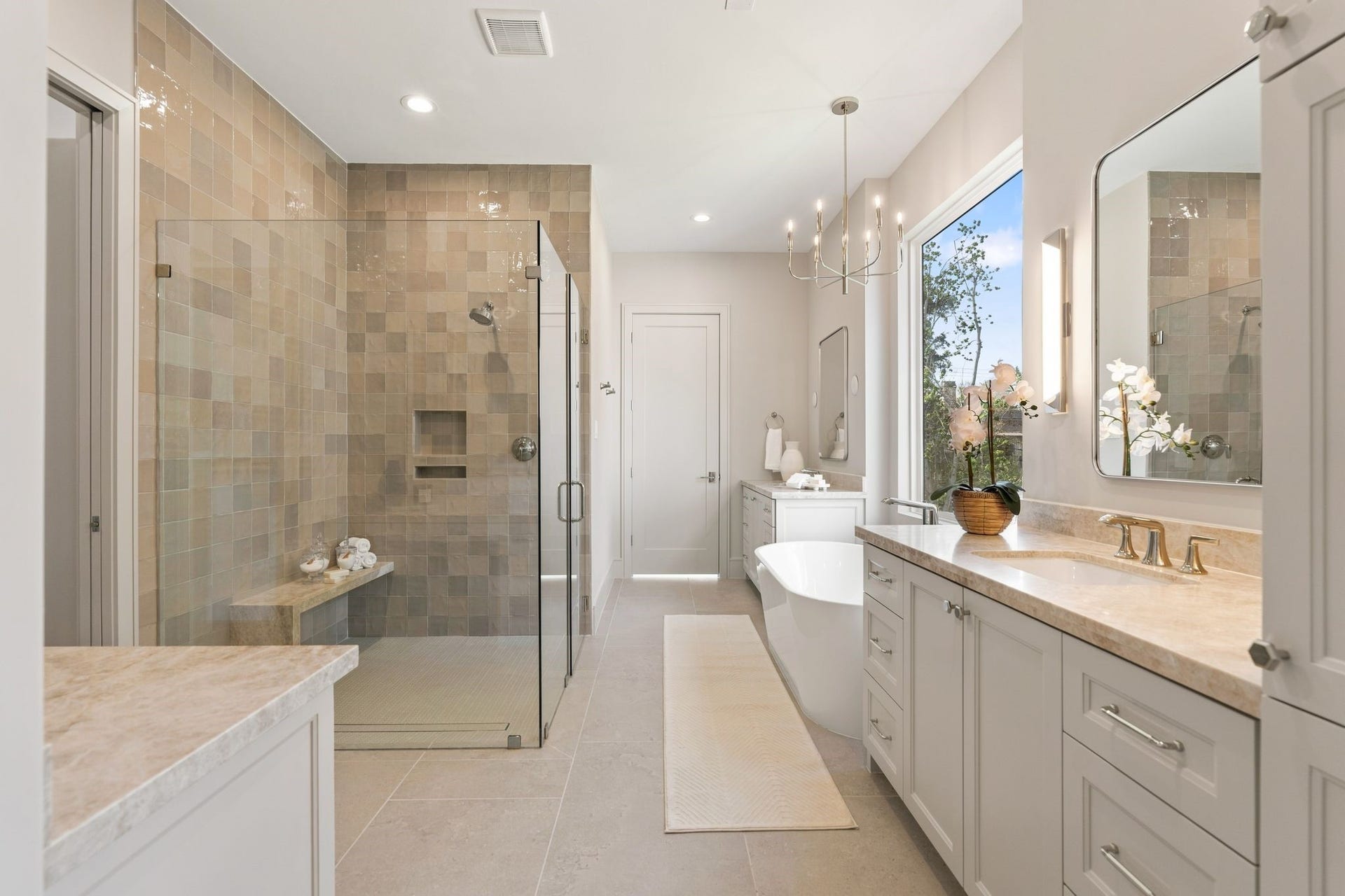 711 E 12th Street, Houston, TX 77008 Warm natural stone and soft lighting give the primary bath a serene, luxurious feel. Taj Mahal quartzite countertops pair with polished nickel Kohler Purist fixtures and glowing alabaster sconces. Double sinks provide convenience and ease both framed with alabaster sconces.