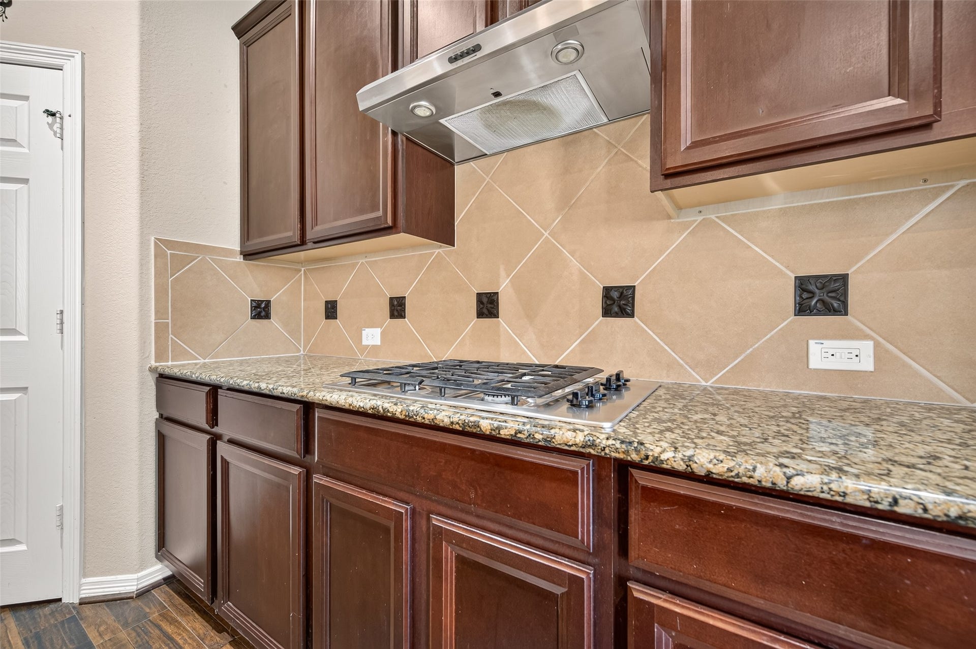 4314 Kent Ranch Court, Katy, TX 77494 Gas cooktop with stainless vent hood and diagonal tile backsplash with decorative accents.