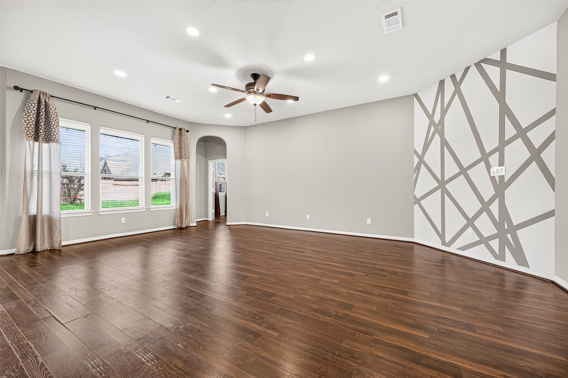 4314 Kent Ranch Court, Katy, TX 77494 Living room with a row of backyard-facing windows, ceiling fan and geometric accent wall.