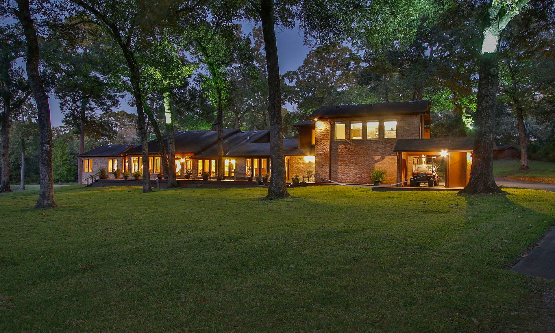 23107 Kobs Road, Tomball, TX 77377 This photo showcases a charming sunset picture, well-lit home nestled among mature trees. The expansive lawn and large windows create an inviting atmosphere, perfect for enjoying serene, natural surroundings.
