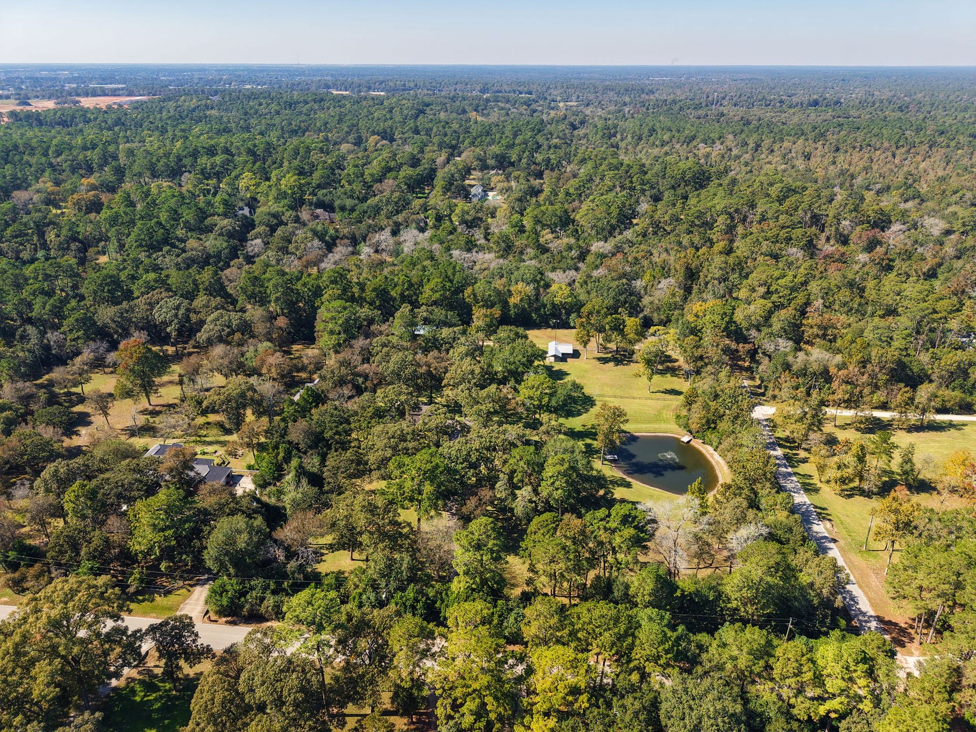 23107 Kobs Road, Tomball, TX 77377 Aerial view of a serene, wooded area featuring a spacious property with a house and pond. The landscape is lush and green, offering privacy and a natural setting, ideal for those seeking tranquility in a rural environment.