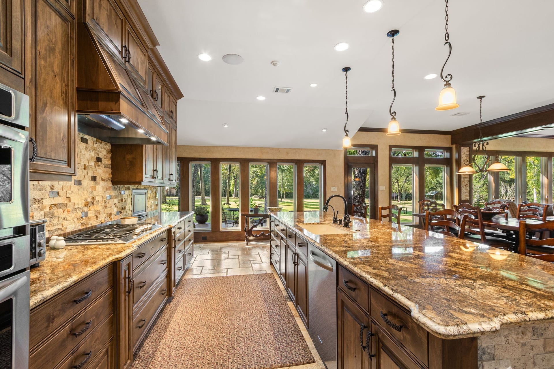 23107 Kobs Road, Tomball, TX 77377 This spacious kitchen features elegant wooden cabinetry, gorgeous granite countertops, pendant lighting, and a large center island. It offers stainless steel appliances, a cozy dining area, and abundant natural light from the large windows overlooking a lush backyard.