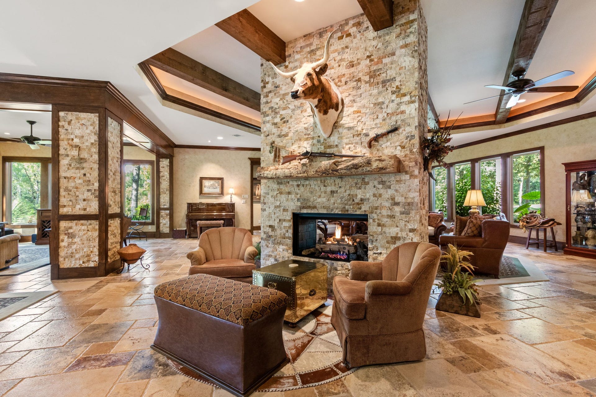 23107 Kobs Road, Tomball, TX 77377 This spacious living area features a rustic stone fireplace, high beamed ceilings, and large windows offering natural light. The open layout connects cozy seating areas, ideal for entertaining with your guests.