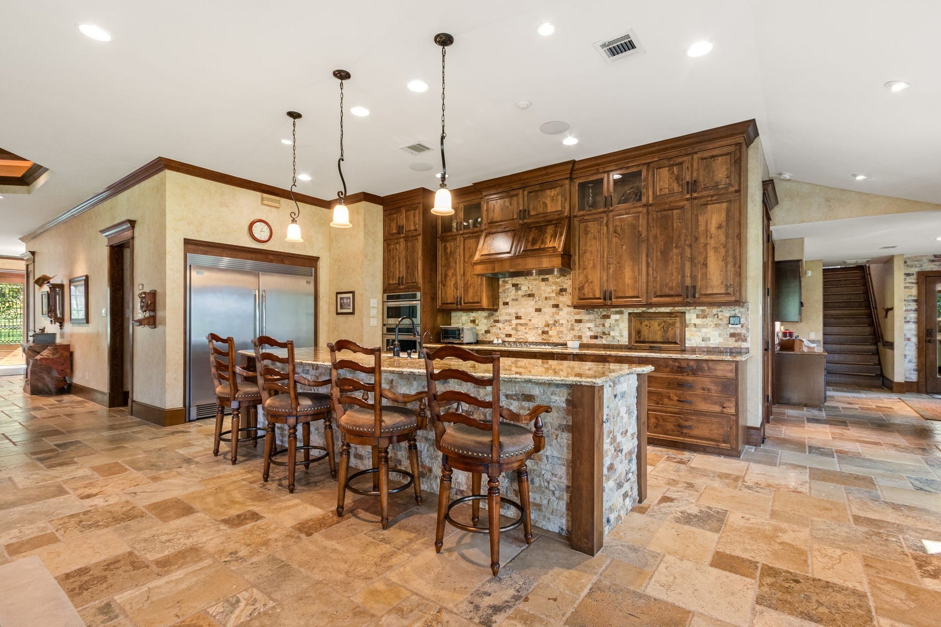 23107 Kobs Road, Tomball, TX 77377 This spacious kitchen features stunning wooden cabinets, a large island with bar seating for your bar stools, and modern stainless steel appliances. The tile flooring and warm lighting create an inviting atmosphere, perfect for entertaining.