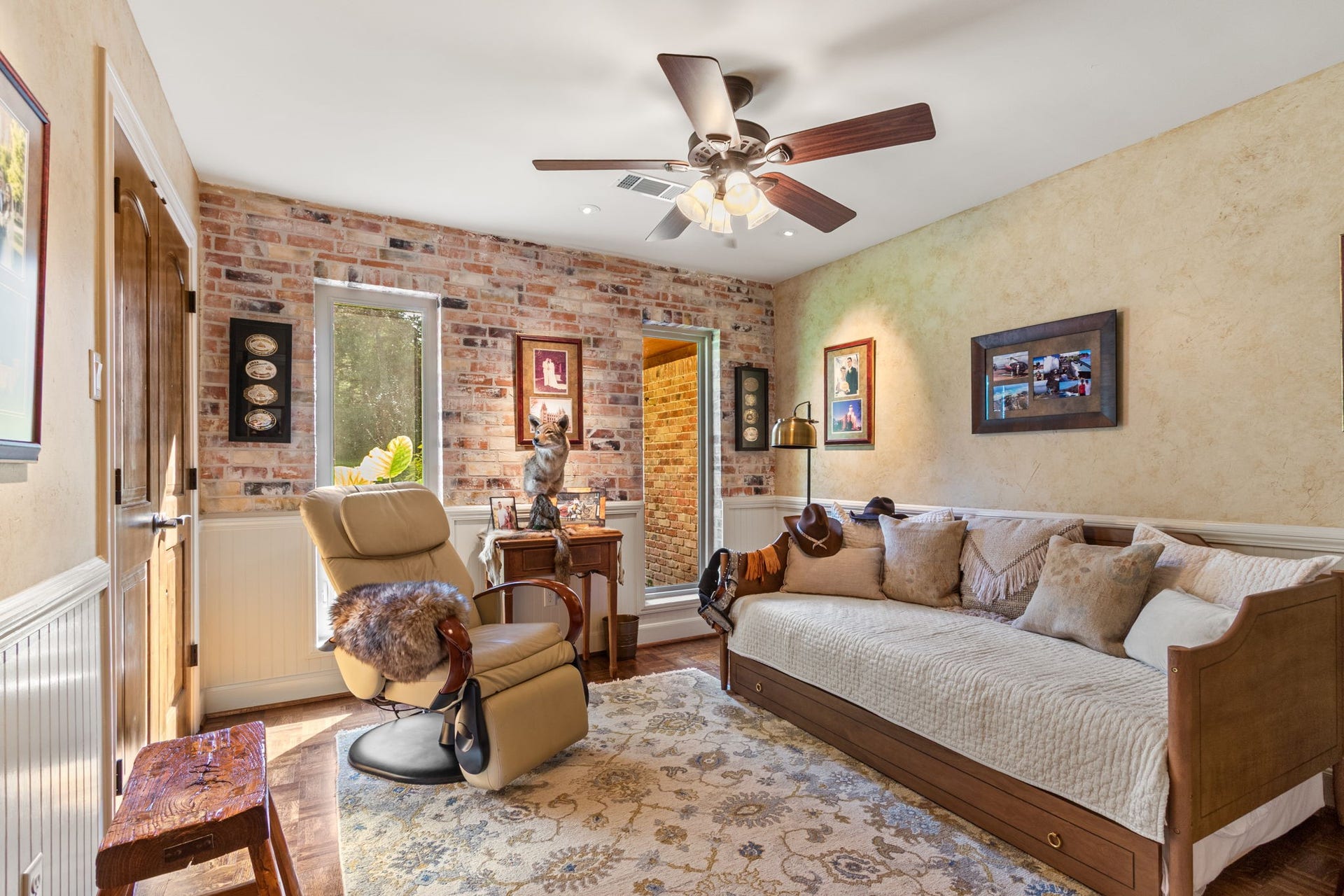 23107 Kobs Road, Tomball, TX 77377 This cozy room features rustic brick accent walls, a comfortable daybed with plush pillows, and a reclining chair. The bedroom is warmly lit with a ceiling fan and has decorative brick accent wall, creating a welcoming atmosphere. Perfect for a cozy retreat or reading nook.