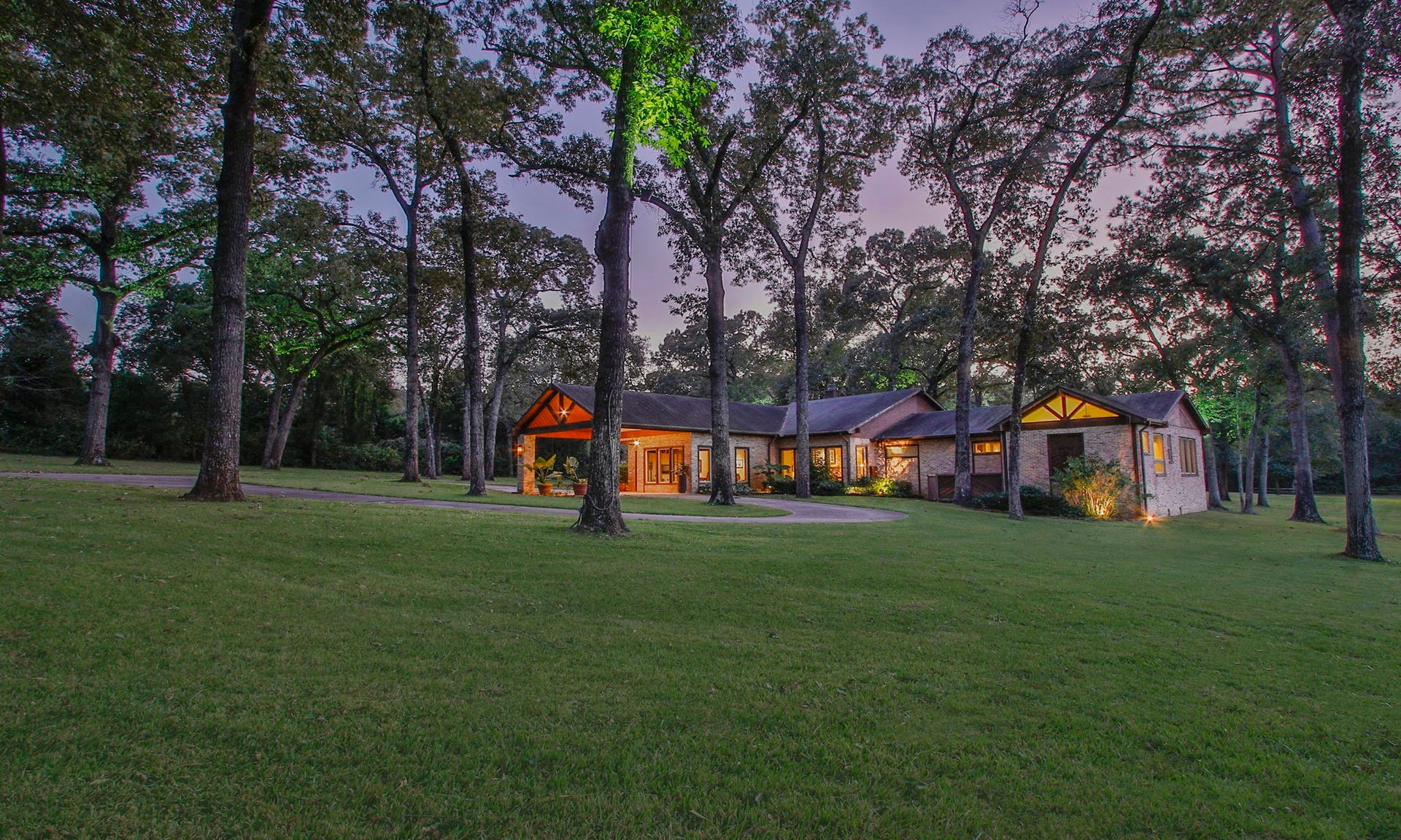 23107 Kobs Road, Tomball, TX 77377 This charming home is nestled among tall trees on a spacious, well-manicured lawn. The warm exterior lighting highlights the inviting architecture, creating a serene and welcoming atmosphere perfect for nature lovers.
