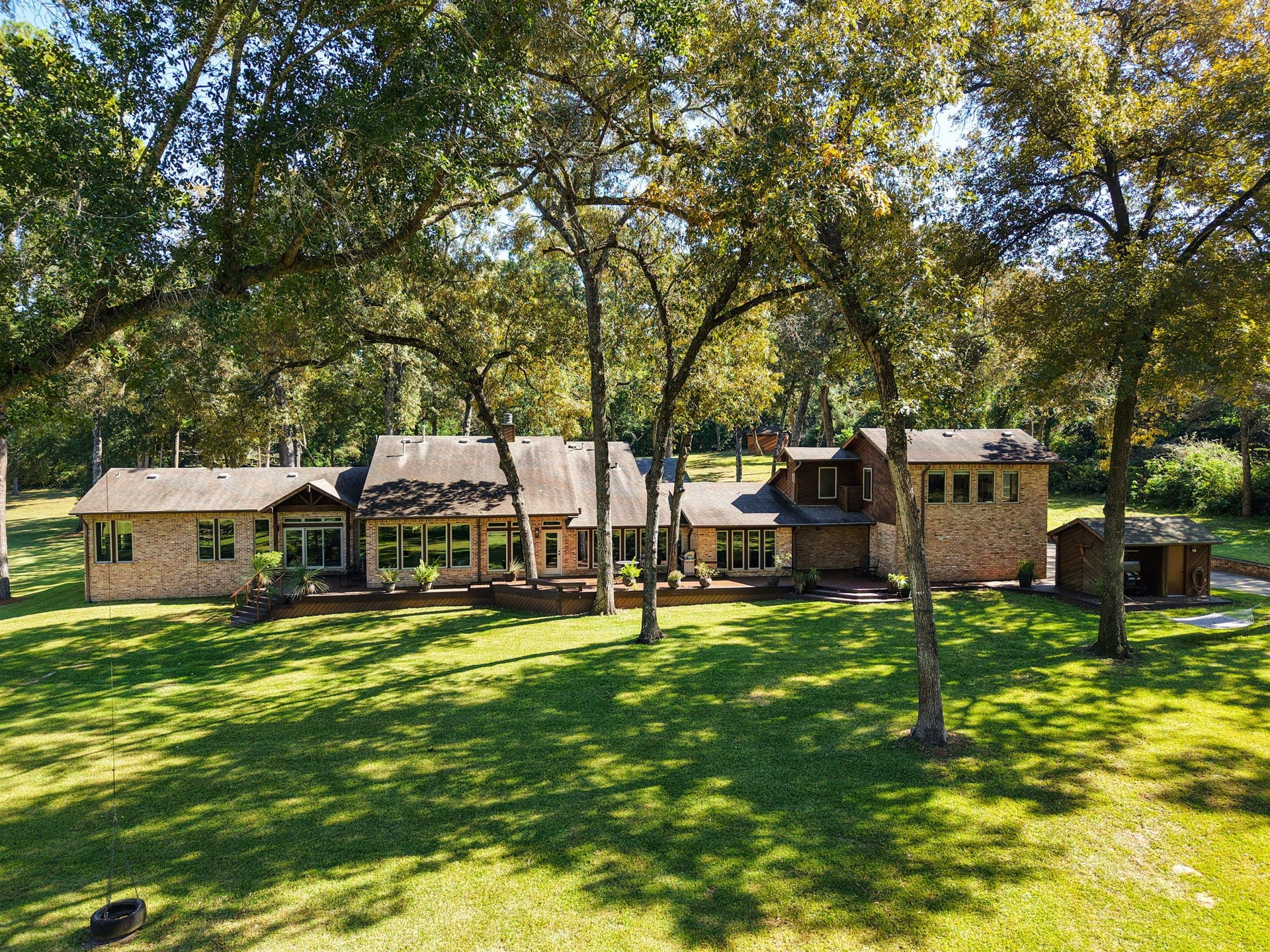 23107 Kobs Road, Tomball, TX 77377 This photo showcases a sprawling, 1.5 story brick home with a multi-level design, nestled among mature trees on a large, well-maintained lawn. The property provides a serene, private atmosphere with ample natural light and a welcoming outdoor space.
