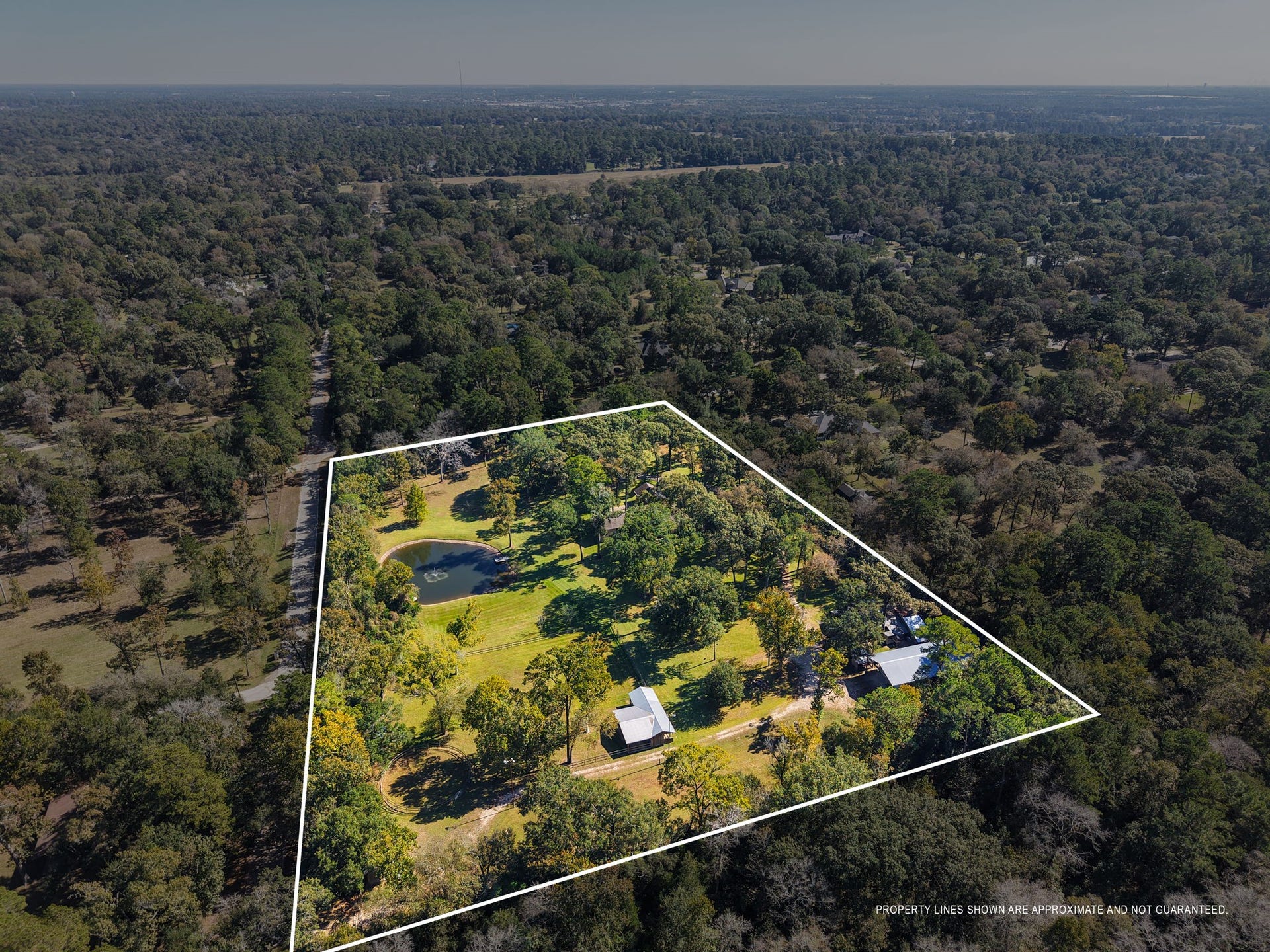 23107 Kobs Road, Tomball, TX 77377 This aerial photo shows a spacious, tree-filled property with a pond and several barns, offering a serene and private setting amid a lush, forested landscape.