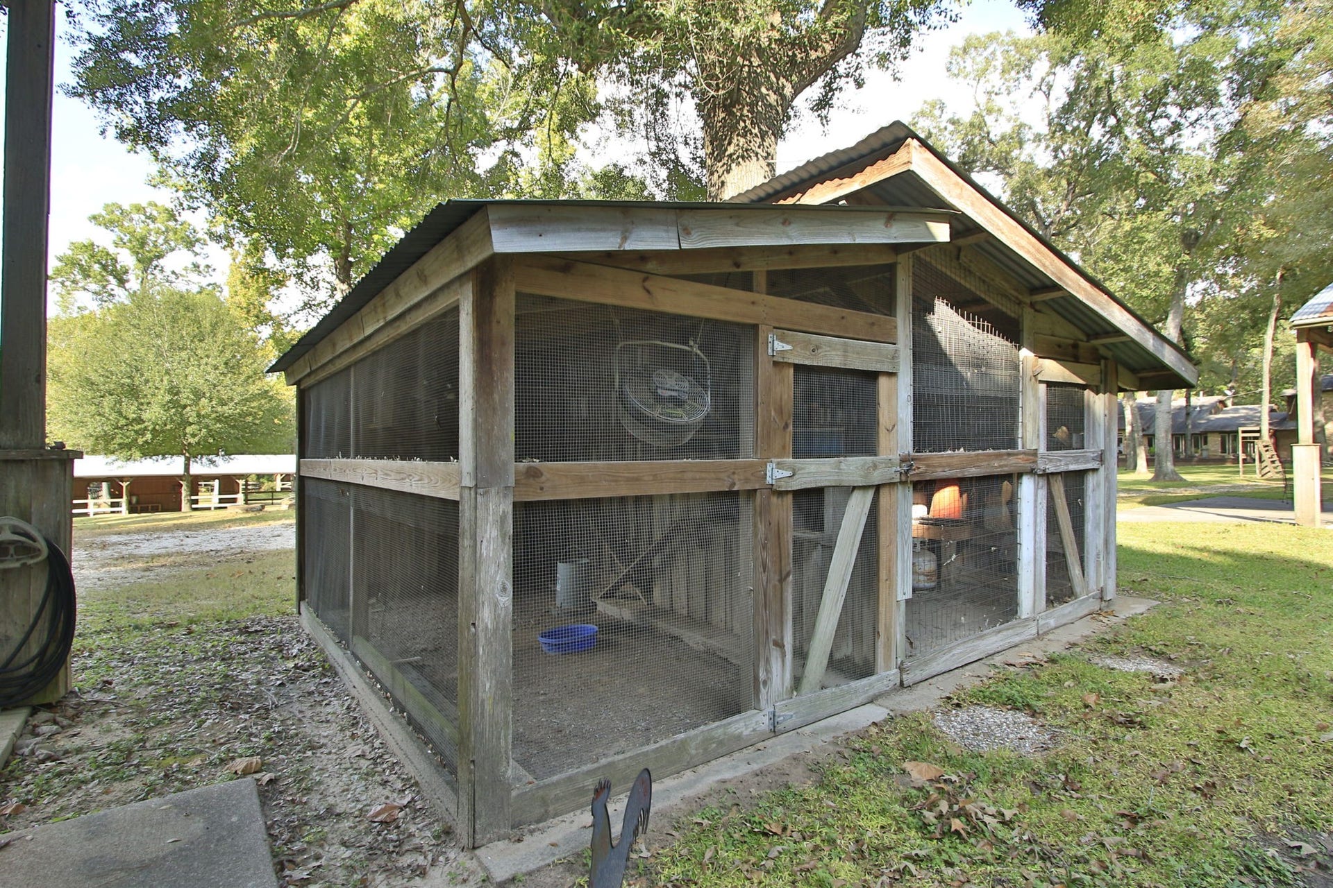23107 Kobs Road, Tomball, TX 77377 This photo shows a sturdy wooden chicken coop with wire mesh, set in a grassy backyard area. It's spacious and shaded by trees, ideal for keeping poultry in a natural environment.