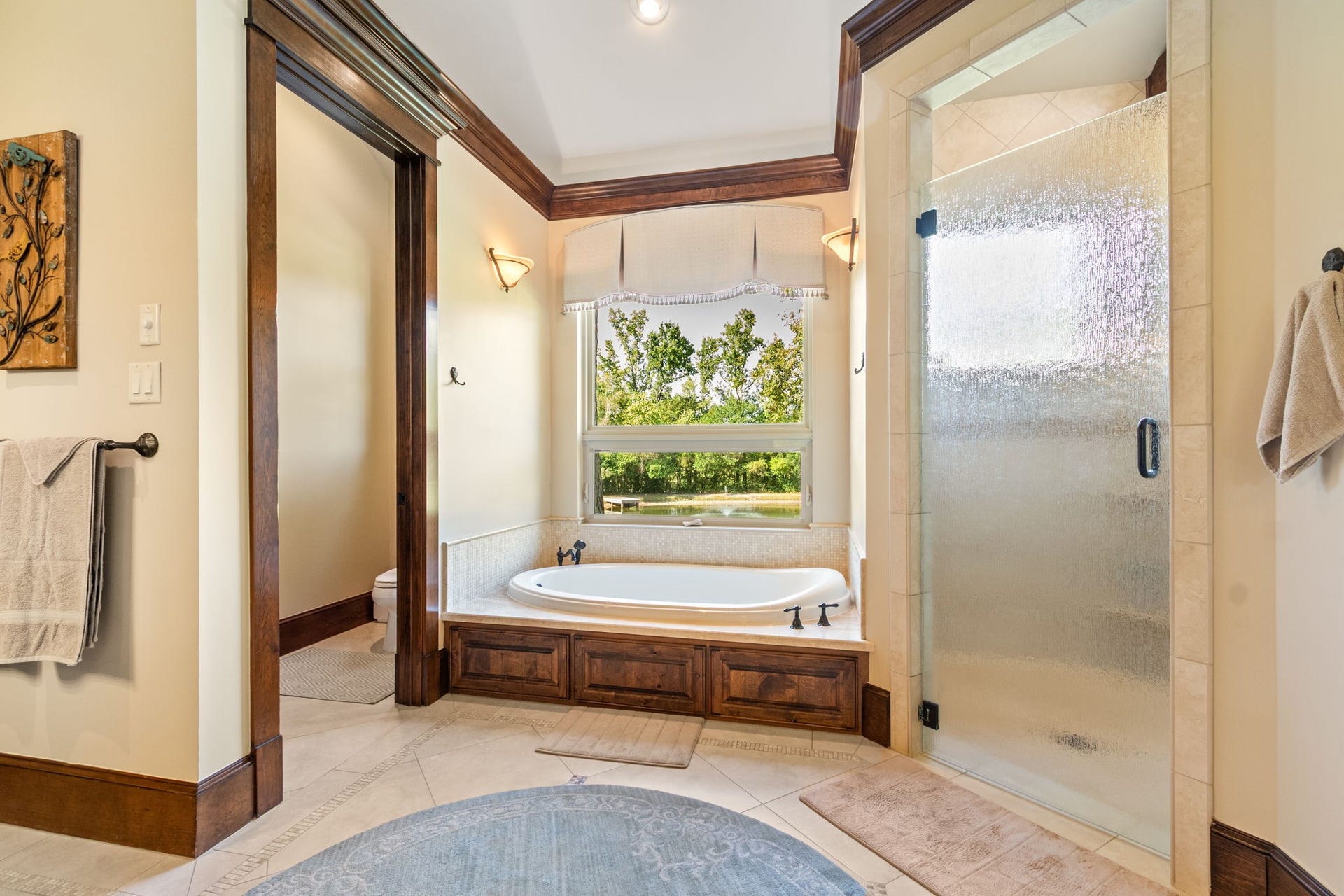 23107 Kobs Road, Tomball, TX 77377 This primary bathroom features a cozy spa-like atmosphere with a large jetted soaking tub. It includes a glass-enclosed shower, elegant wood trim, and stylish light fixtures, creating a serene and inviting space.