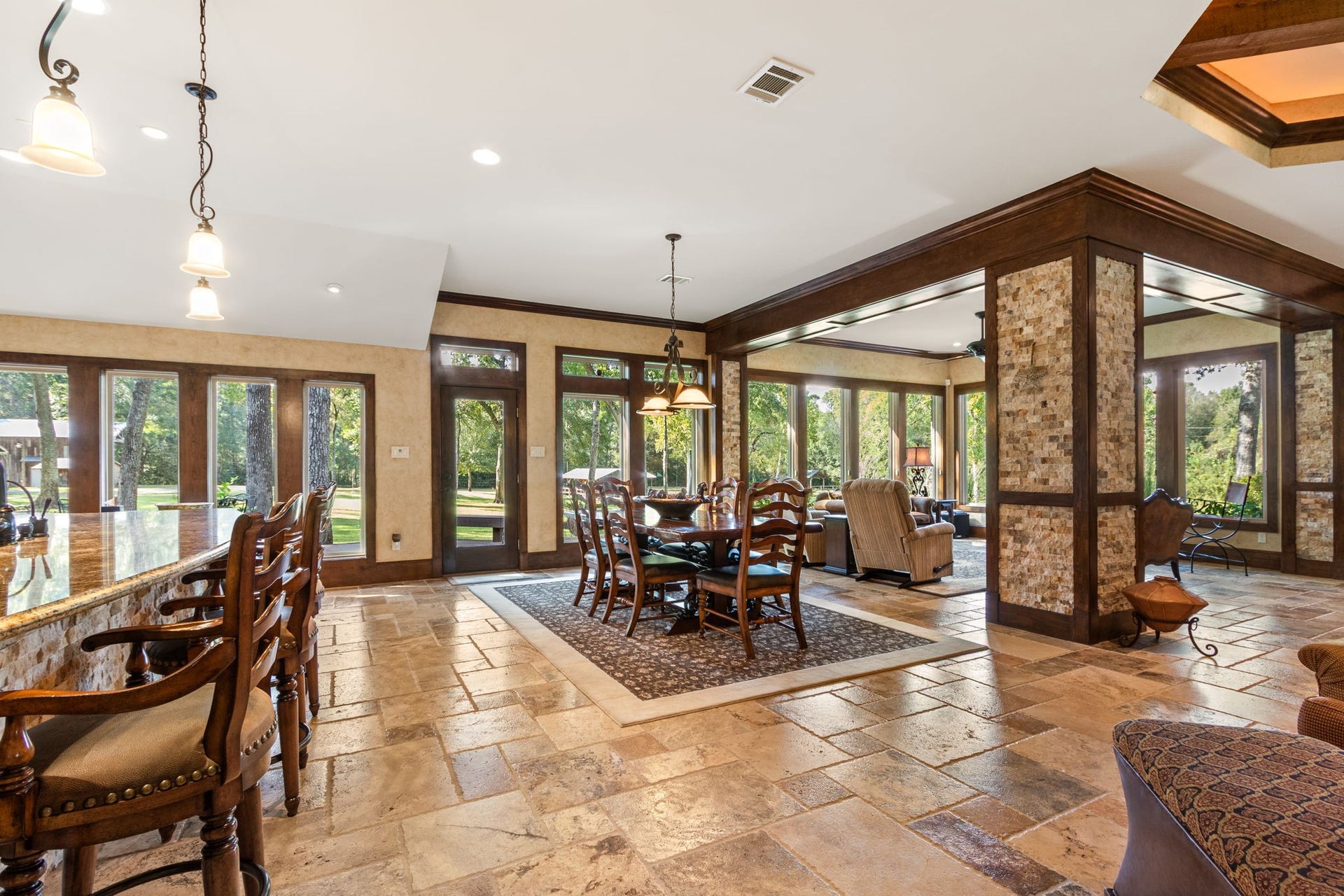 23107 Kobs Road, Tomball, TX 77377 This open-concept living space features large windows with panoramic views, elegant travertine flooring, and a cozy dining area. The room is accented with warm wood tones and stylish lighting, creating an inviting atmosphere.