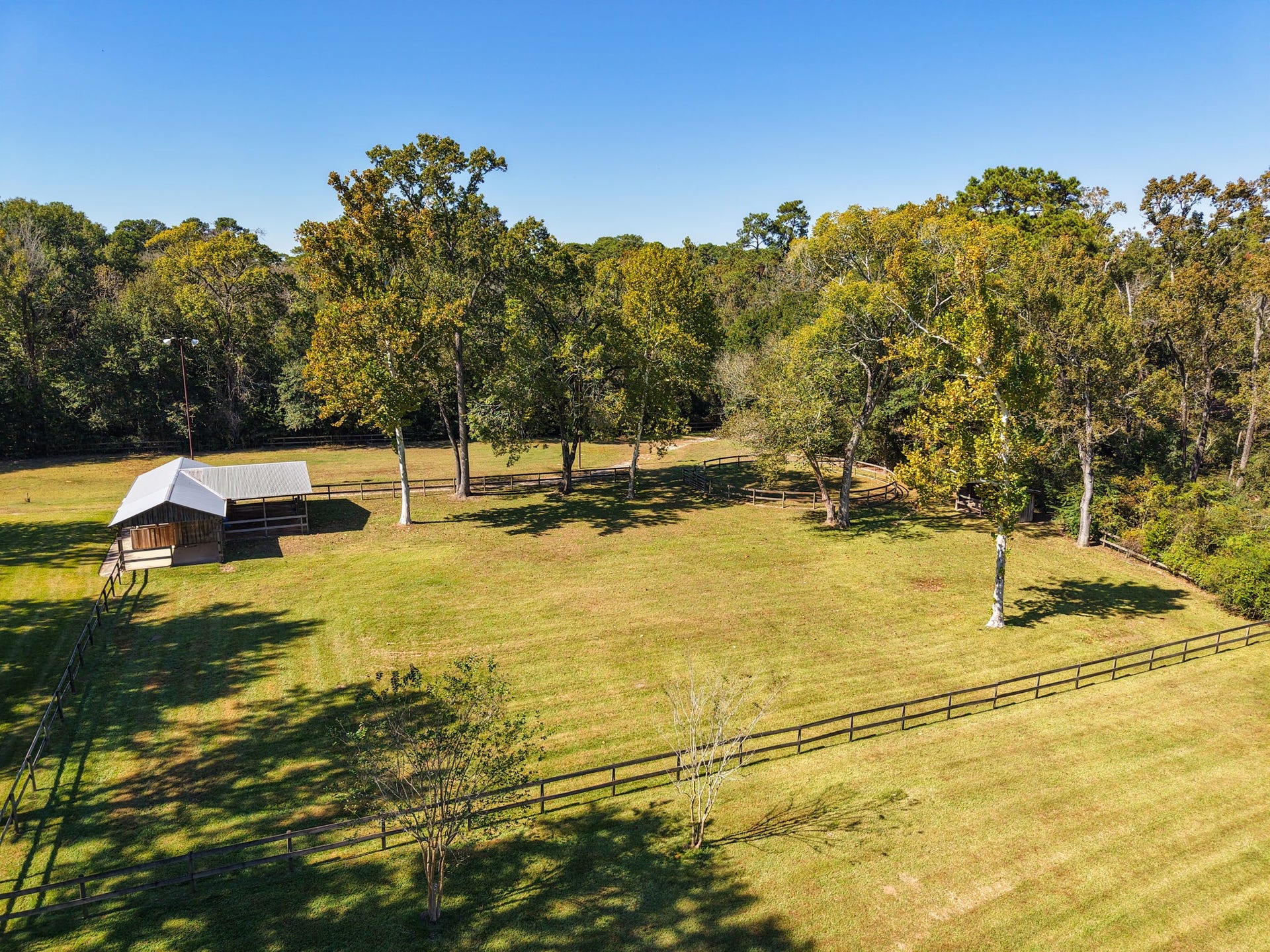23107 Kobs Road, Tomball, TX 77377 This photo showcases a spacious, fenced pasture with a barn, surrounded by mature trees and open green space, ideal for outdoor activities and livestock.