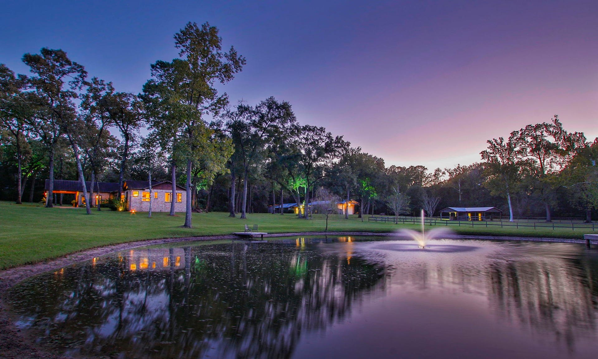 23107 Kobs Road, Tomball, TX 77377 This serene property features a charming home surrounded by trees, with a beautifully lit pond and fountain. The peaceful setting is ideal for enjoying tranquil sunsets and natural beauty.
