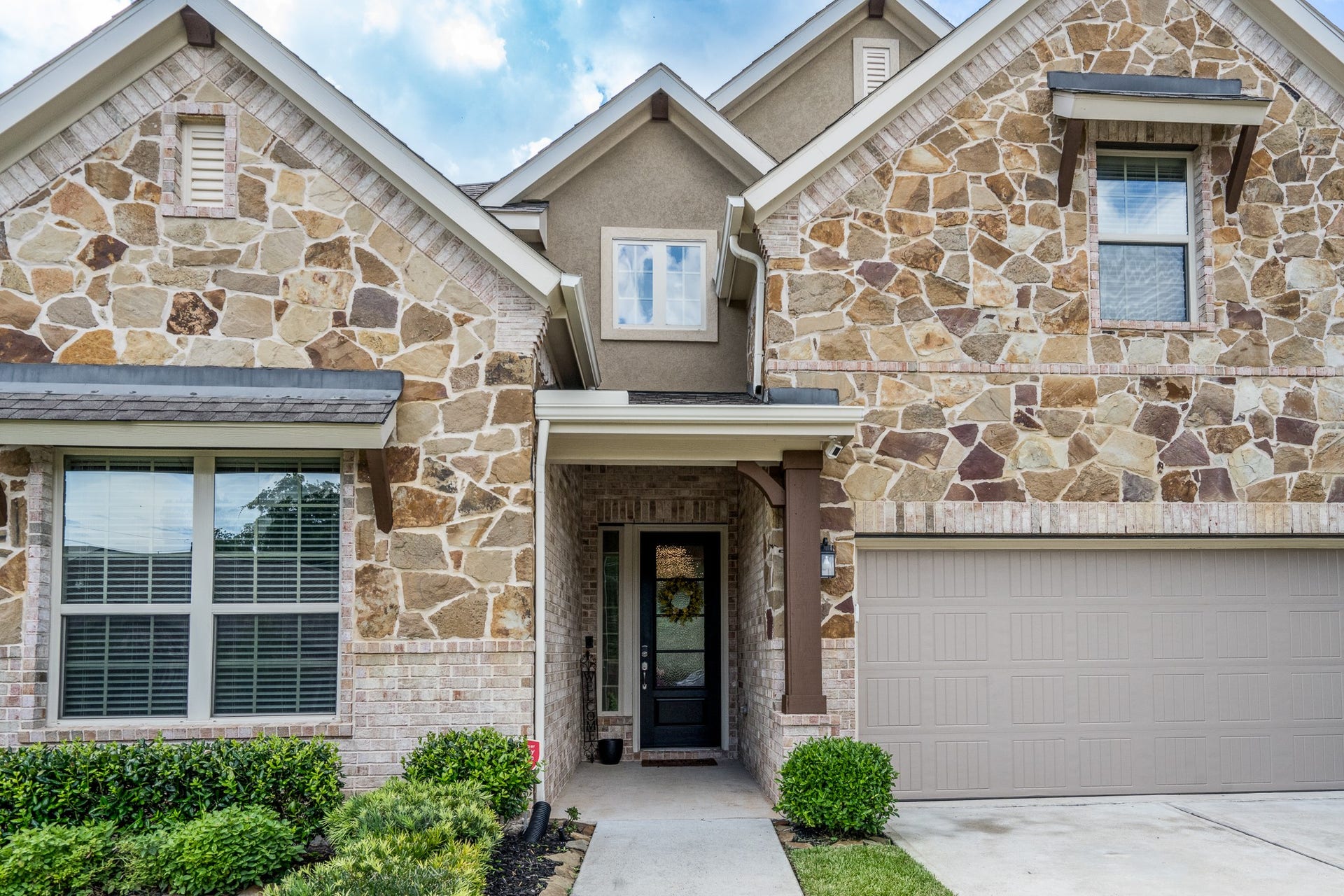 Charming two-story home with a beautiful stone facade and inviting front entrance, featuring a spacious garage and well-maintained landscaping.