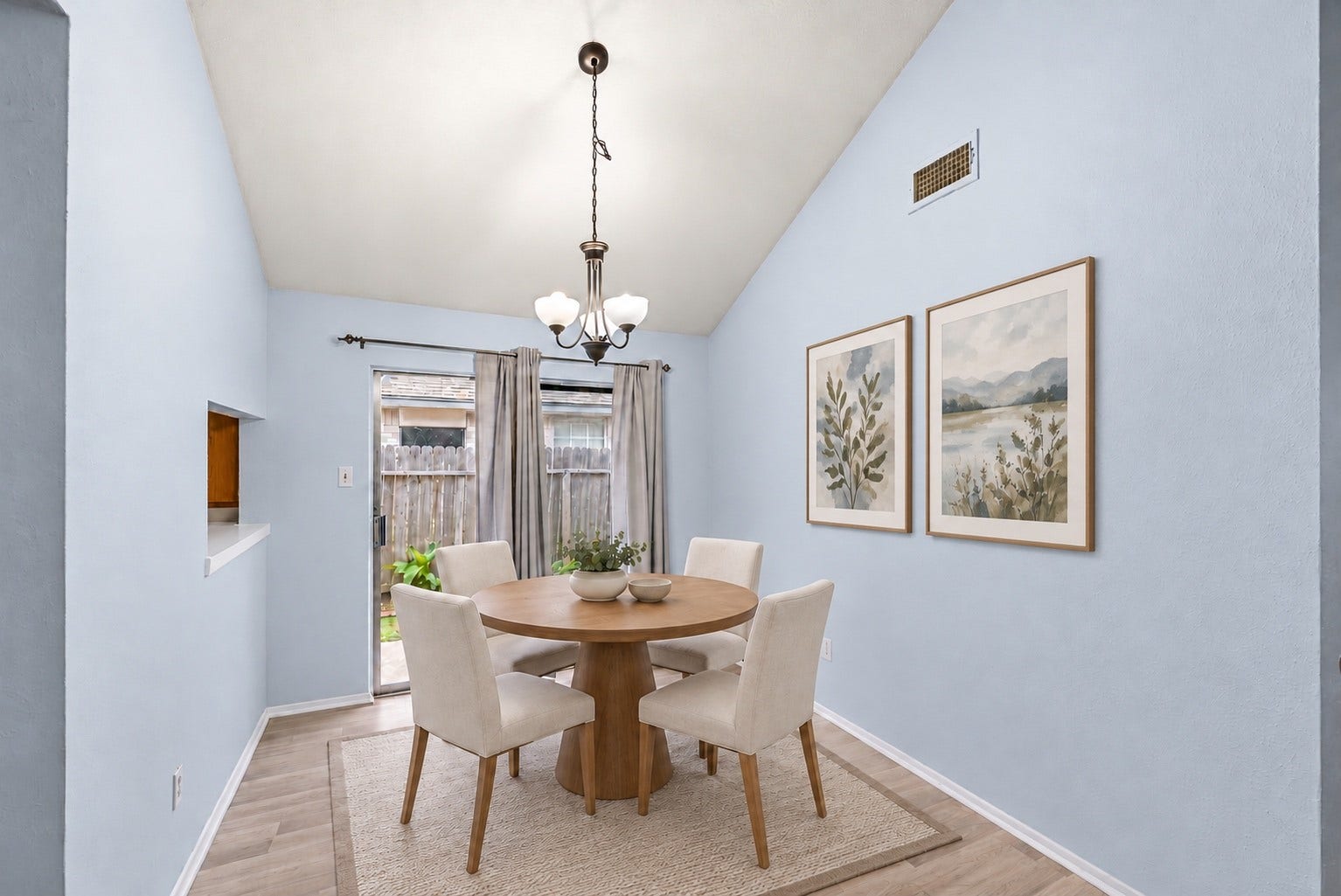 Right off the back patio, the 10'7" x 9'1" Dining Area opens to the yard through a sliding glass door. A wall opening on the left looks through to the Kitchen counter for passing plates. The hanging light fixture is centered over the table spot, and curtains are already hung on the slider. Wood-look flooring runs right up to the glass, and light walls with white baseboards keep the room bright. On a nice evening, dinner can move straight out to the patio and lawn! Virtually staged.