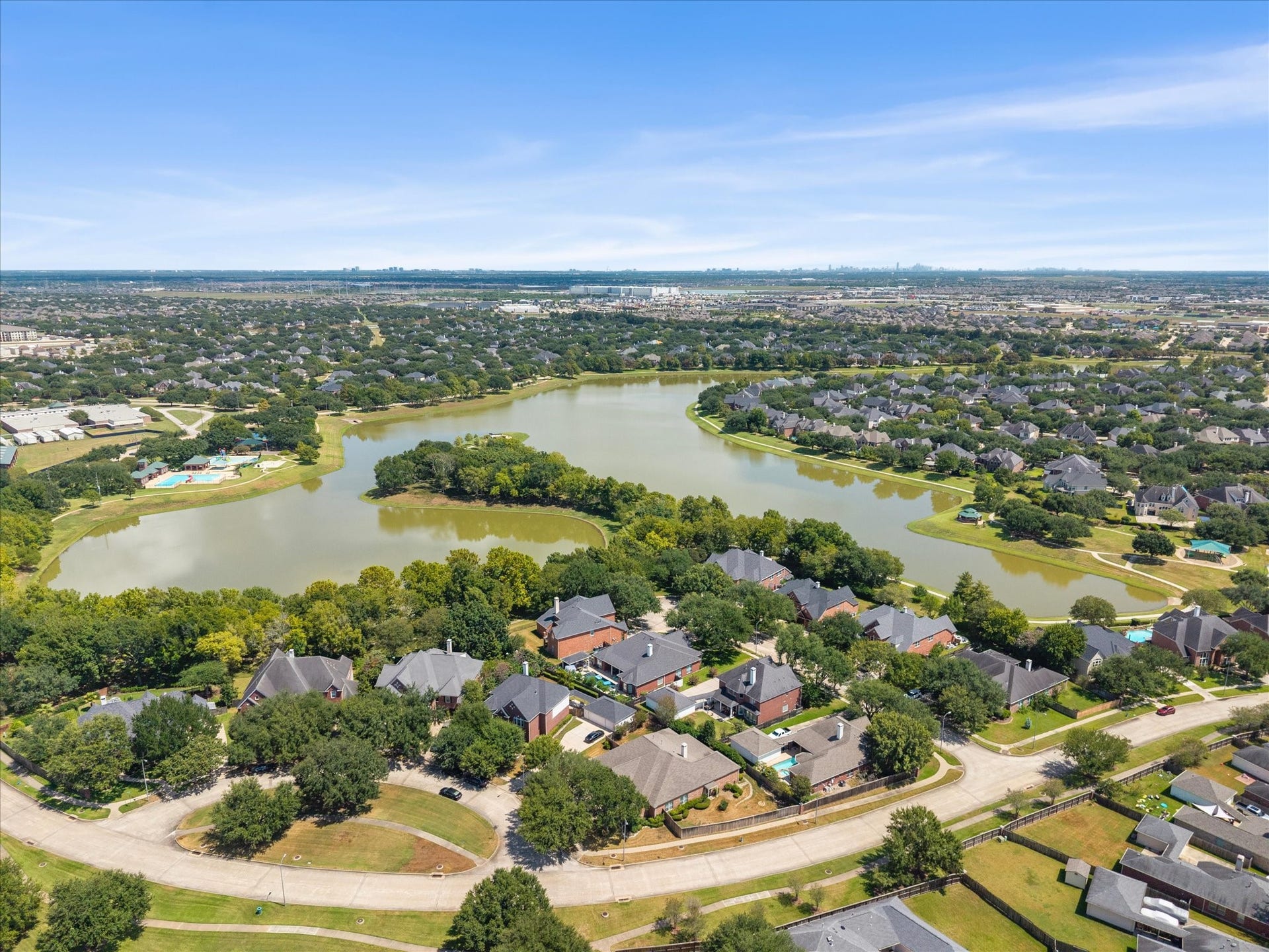 1834 Lake Quitman Drive, Richmond, TX 77406 Beautiful aerial view showcasing the home's location near Figure Four Lake, with mature tree lined streets, community amenities, and the Houston skyline in the distance.