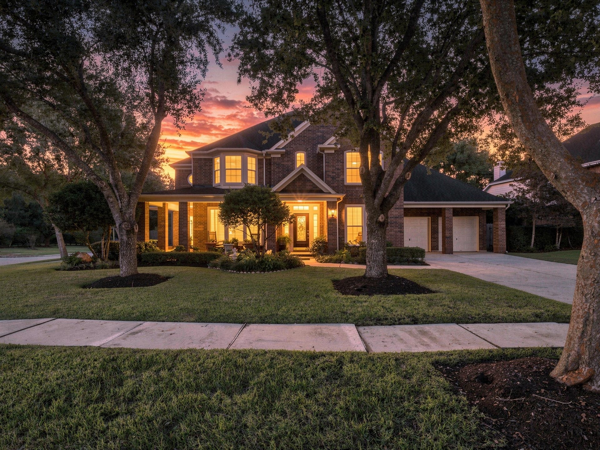 1834 Lake Quitman Drive, Richmond, TX 77406 Gorgeous twilight curb appeal. Brick two story beautifully lit against a vivid sunset, framed by mature trees and manicured landscaping.