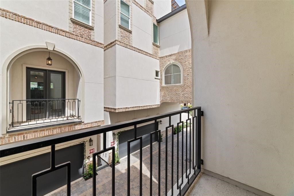 This photo showcases a small balcony with a black metal railing, overlooking a courtyard area with brick and stucco building facades. The view includes arched windows and doors, adding a touch of architectural charm.