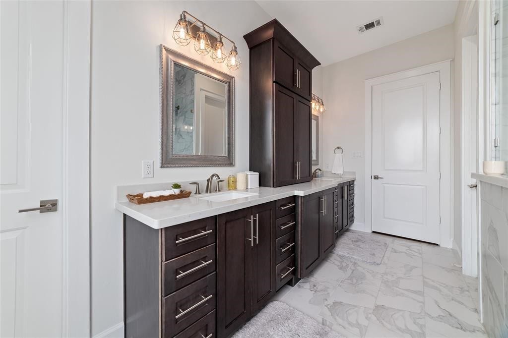 This bathroom features elegant dark wood cabinetry with ample storage, dual sinks, and modern fixtures. The space is brightened by stylish lighting and complemented by a sleek, neutral tile floor.