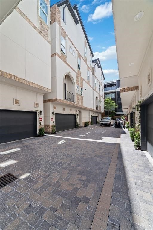 The modern townhouse complex with multi-story units featuring brick and stucco exteriors. The cobblestone driveway leads to multiple garages, offering ample parking. The space is clean and well-maintained, with some greenery adding a touch of nature.