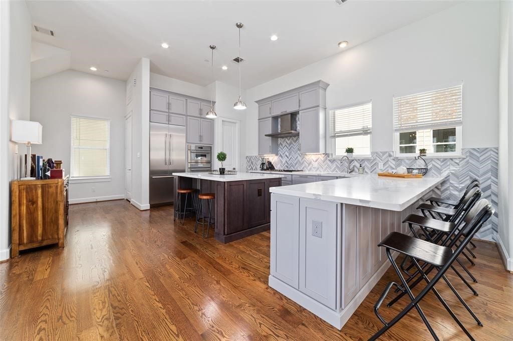 This modern kitchen features sleek cabinetry, a large center island, stainless steel appliances, and stylish herringbone backsplash. The open layout with hardwood floors and ample natural light creates an inviting space for cooking and entertaining.