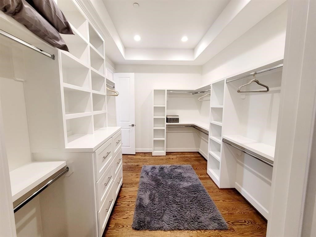 Spacious walk-in closet featuring white shelving, drawers, and hanging racks, with hardwood flooring and recessed lighting. A cozy rug adds warmth.