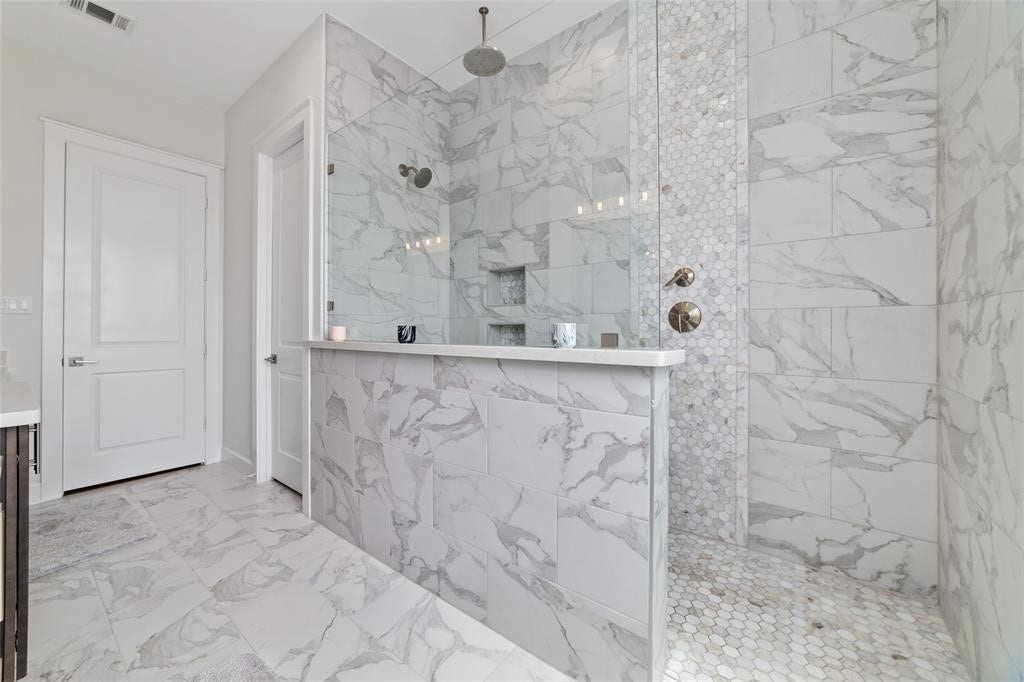 This modern bathroom with elegant marble tile throughout, featuring a spacious walk-in shower with a glass enclosure and stylish fixtures.