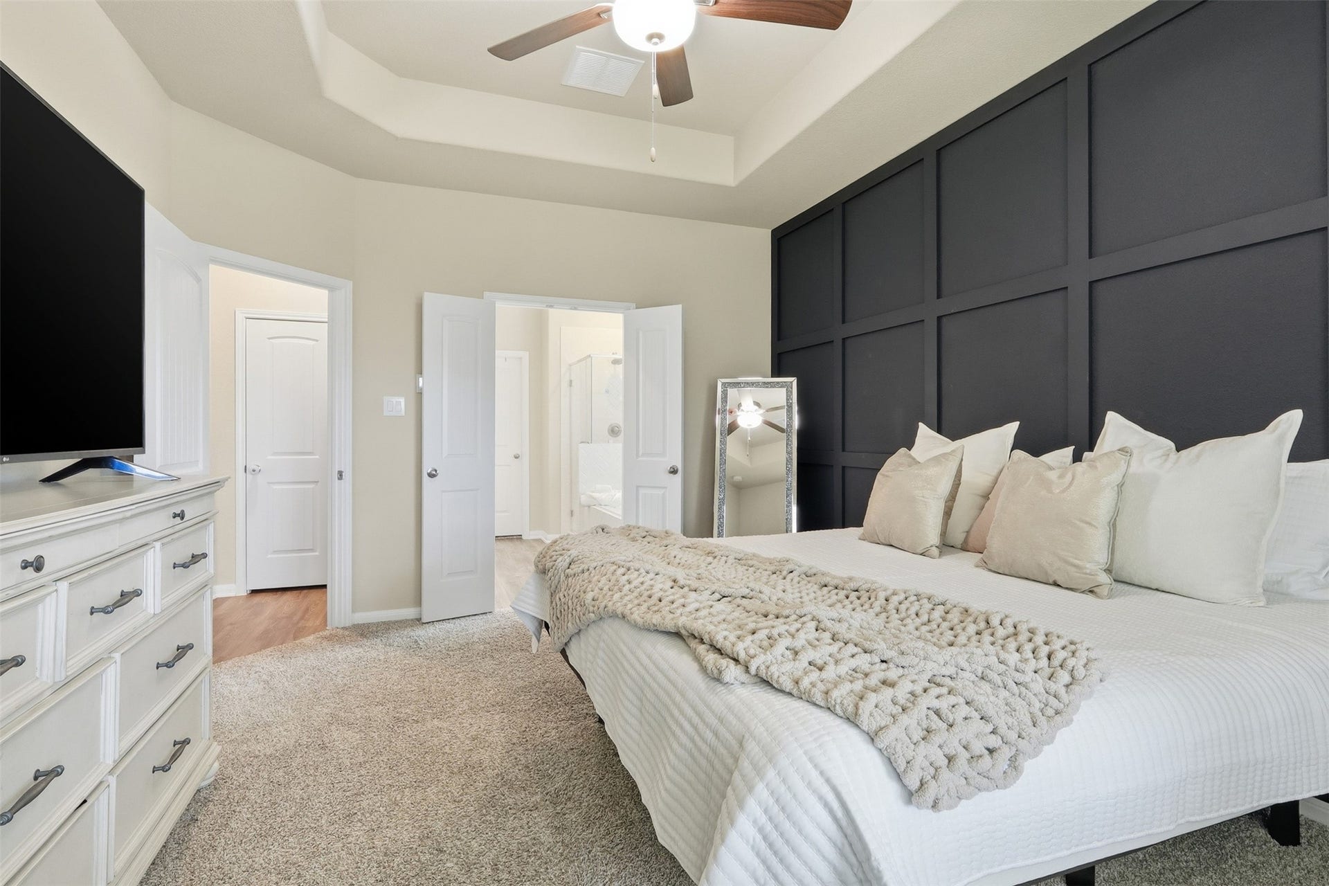 Private primary retreat featuring a stylish accent wall, plush carpeting, ceiling fan, and direct access to the luxurious en-suite bathroom.