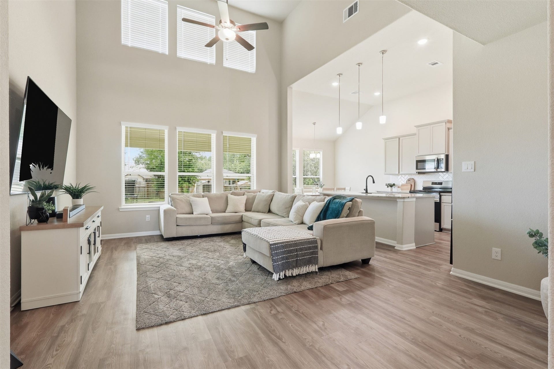 Spacious open-concept living area featuring soaring ceilings, luxury vinyl plank flooring, abundant natural light, and seamless flow into the kitchenperfect for everyday living and entertaining.