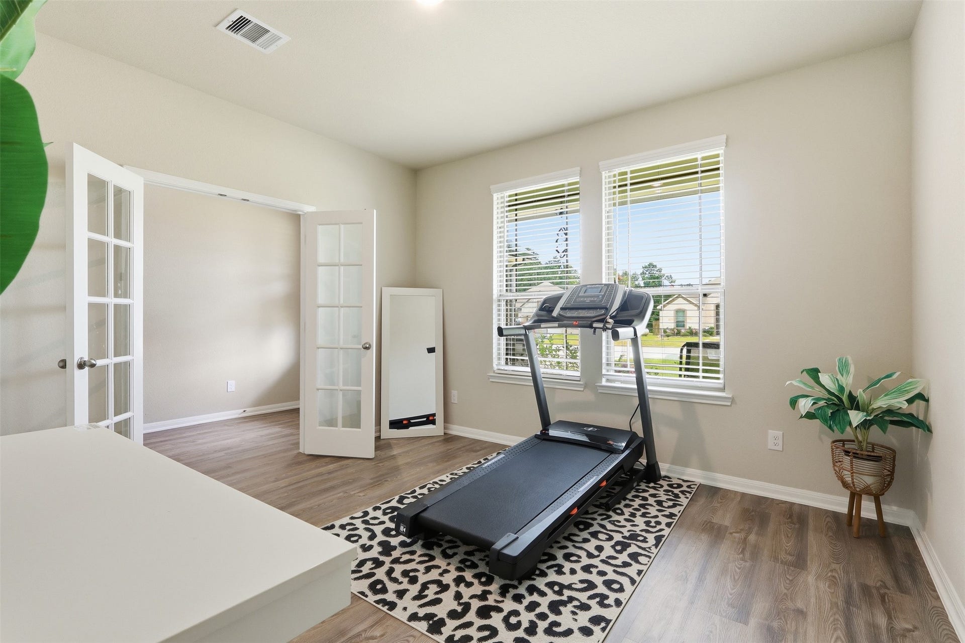 Flexible home office or study featuring elegant French doors, wood flooring, and large windows that fill the space with natural light.