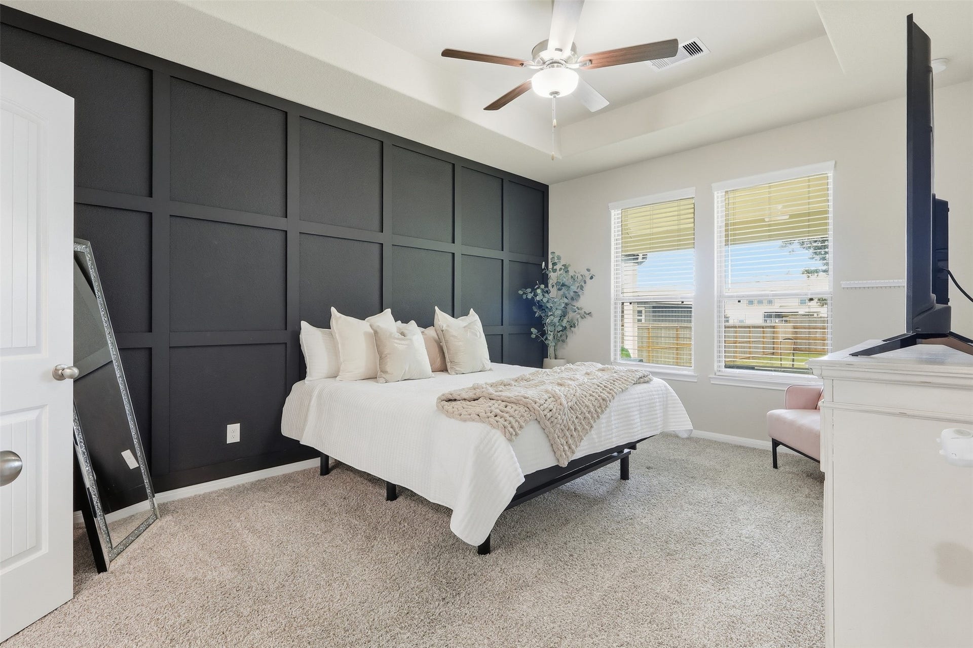 Spacious primary suite featuring a tray ceiling, striking accent wall, ceiling fan, and large windows that provide abundant natural light.