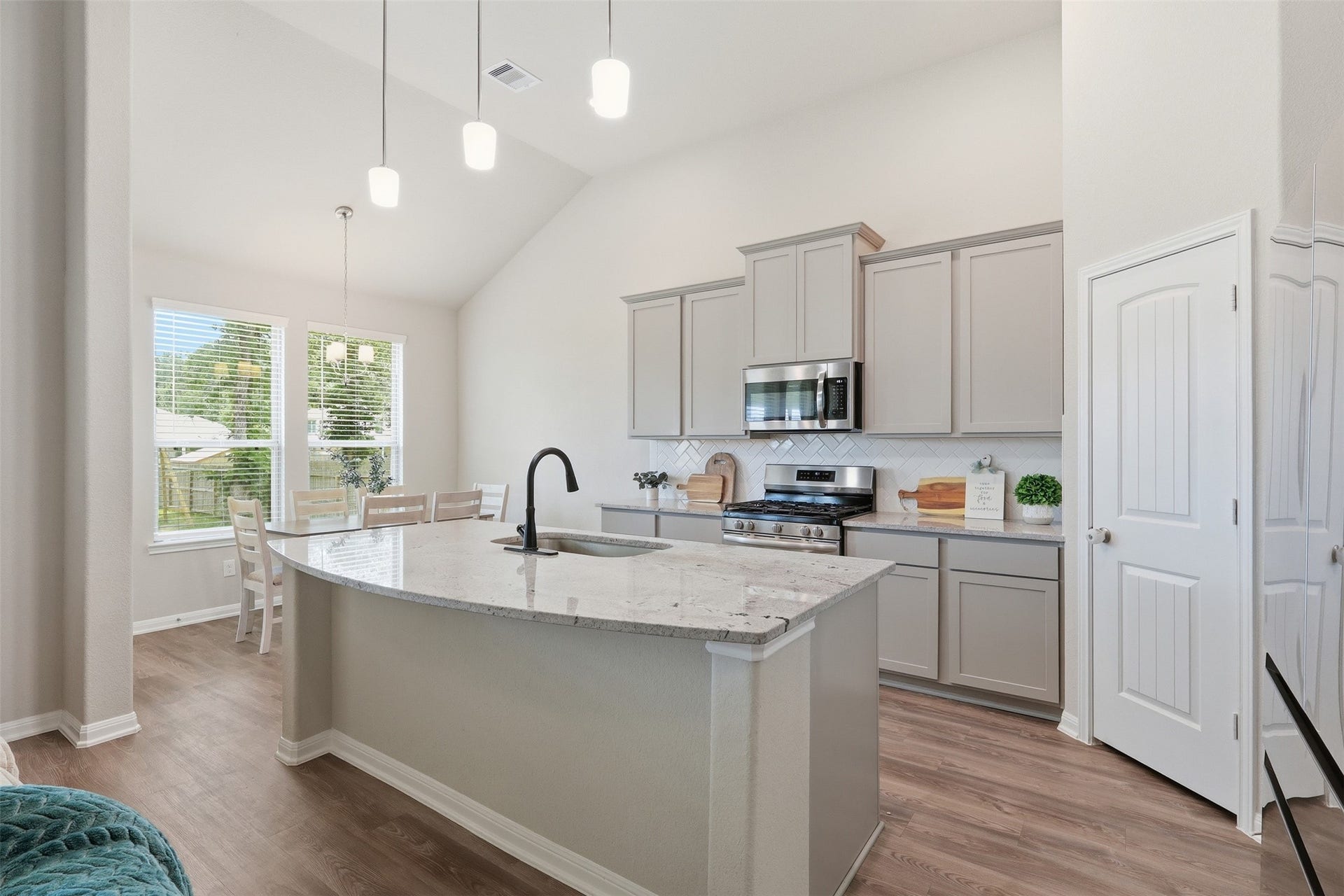 Chef-inspired kitchen featuring a large island, stainless steel appliances, upgraded cabinetry, high ceilings, and a bright dining area filled with natural light.