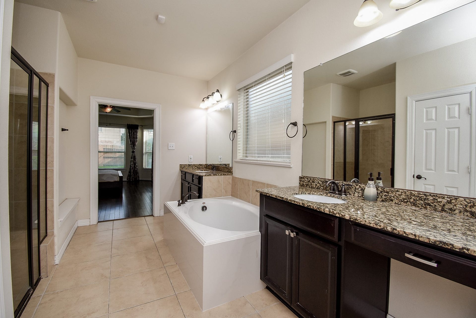 27807 Ashbrook Falls Court, Fulshear, TX 77441 Spacious bathroom with a large soaking tub, granite countertops, dual sinks, and a separate glass-enclosed shower.