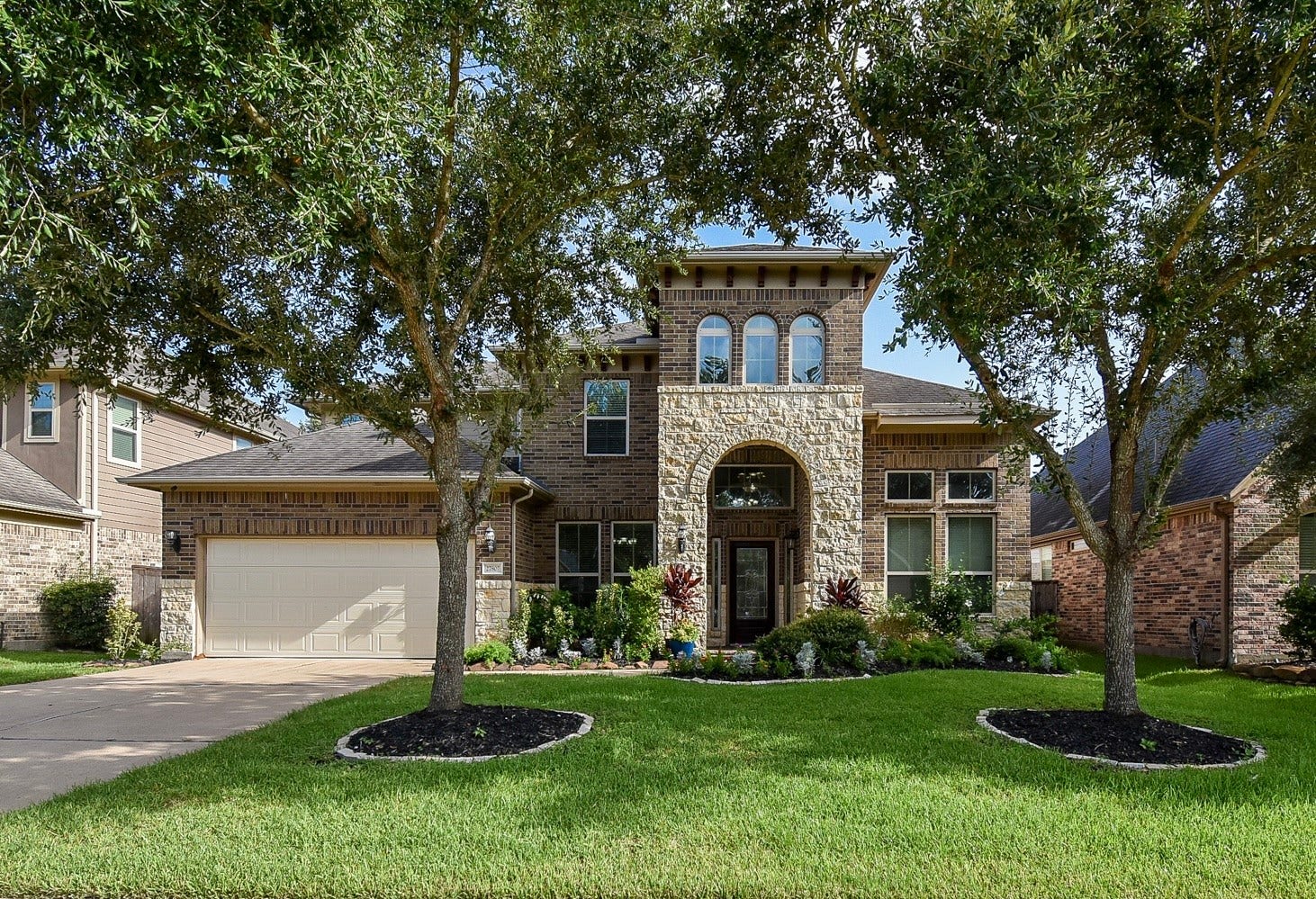 27807 Ashbrook Falls Court, Fulshear, TX 77441 A beautiful two-story home with a stone and brick exterior. Features a spacious driveway, and a 3-car garage. The arched entryway adds elegance to the facade.
