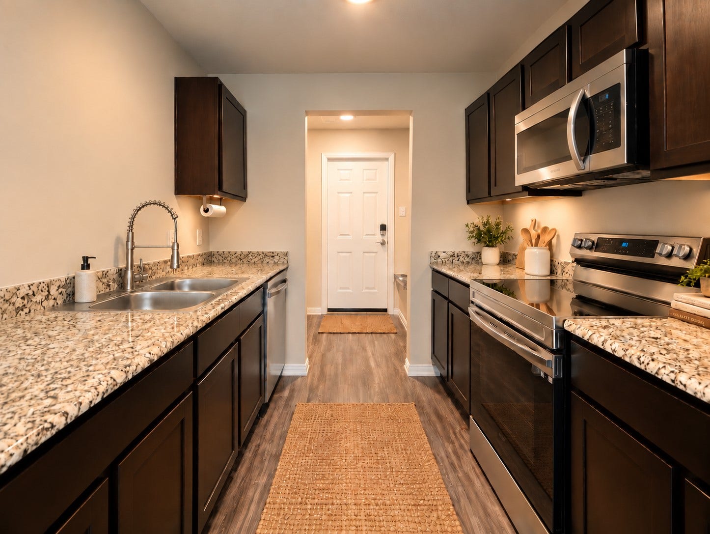 Functional galley kitchen featuring granite countertops, dark cabinetry, and stainless steel appliances.