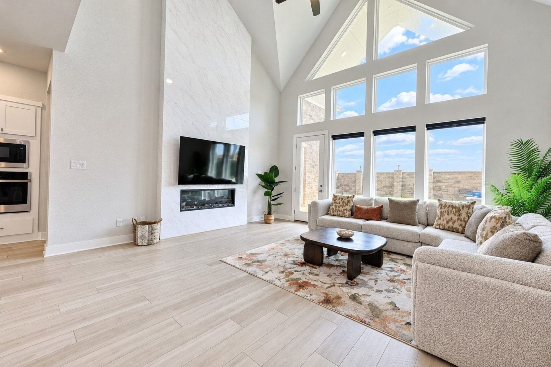 29651 Bur Creek Lane, Fulshear, TX 77441 The spacious two-story living room features a soaring vaulted ceiling, a ceiling fan, luxury vinyl plank flooring, and a modern electric fireplace. Expansive windows fill the space with natural light, creating a bright and inviting atmosphere.