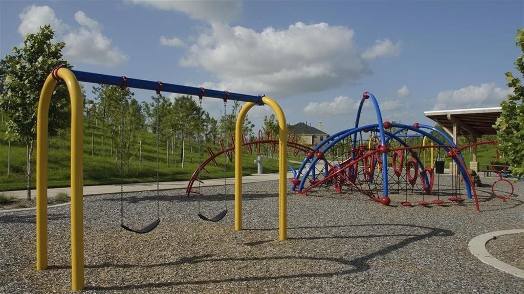 29651 Bur Creek Lane, Fulshear, TX 77441 Another community playground featuring colorful swings and climbing structures, set against a backdrop of lush greenery and open skies. Perfect for family fun and outdoor activities.