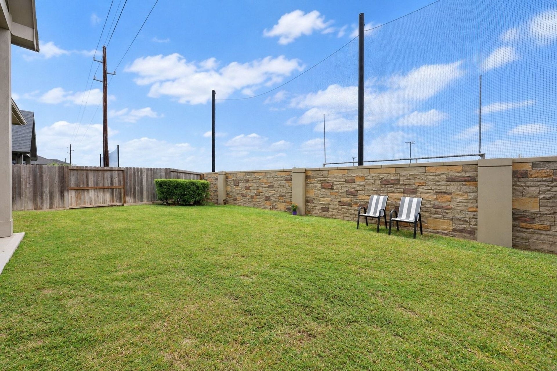 29651 Bur Creek Lane, Fulshear, TX 77441 Spacious backyard with lush green lawn, privacy fencing, and a charming stone wall, perfect for relaxation or outdoor activities.
