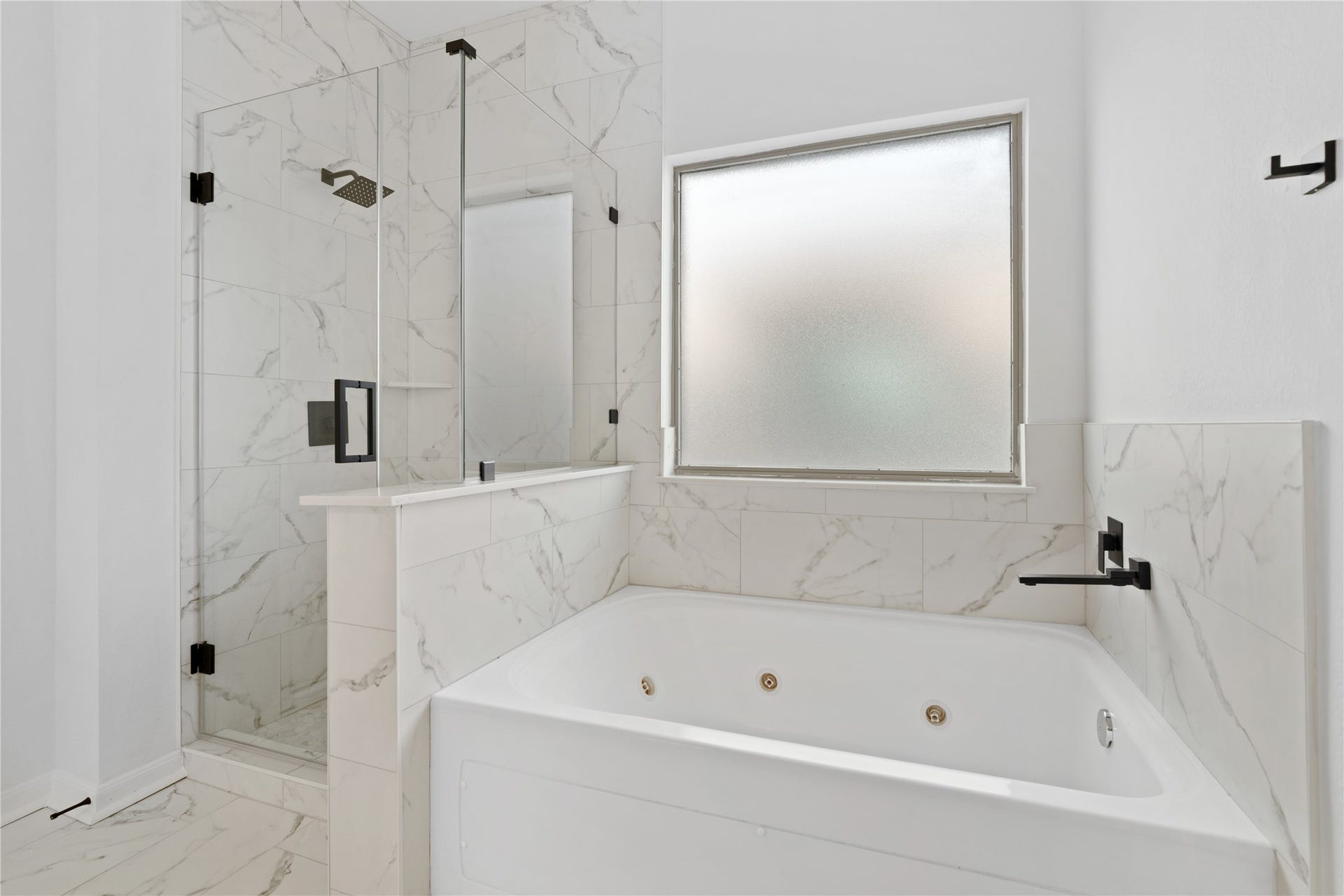 21611 Manitou Falls Lane, Katy, TX 77449 Primary Bathroom Relaxing bath area features a jetted soaking tub, separate glass-enclosed shower, marble-look tile surrounds, matte-black fixtures, and a privacy-glass window.