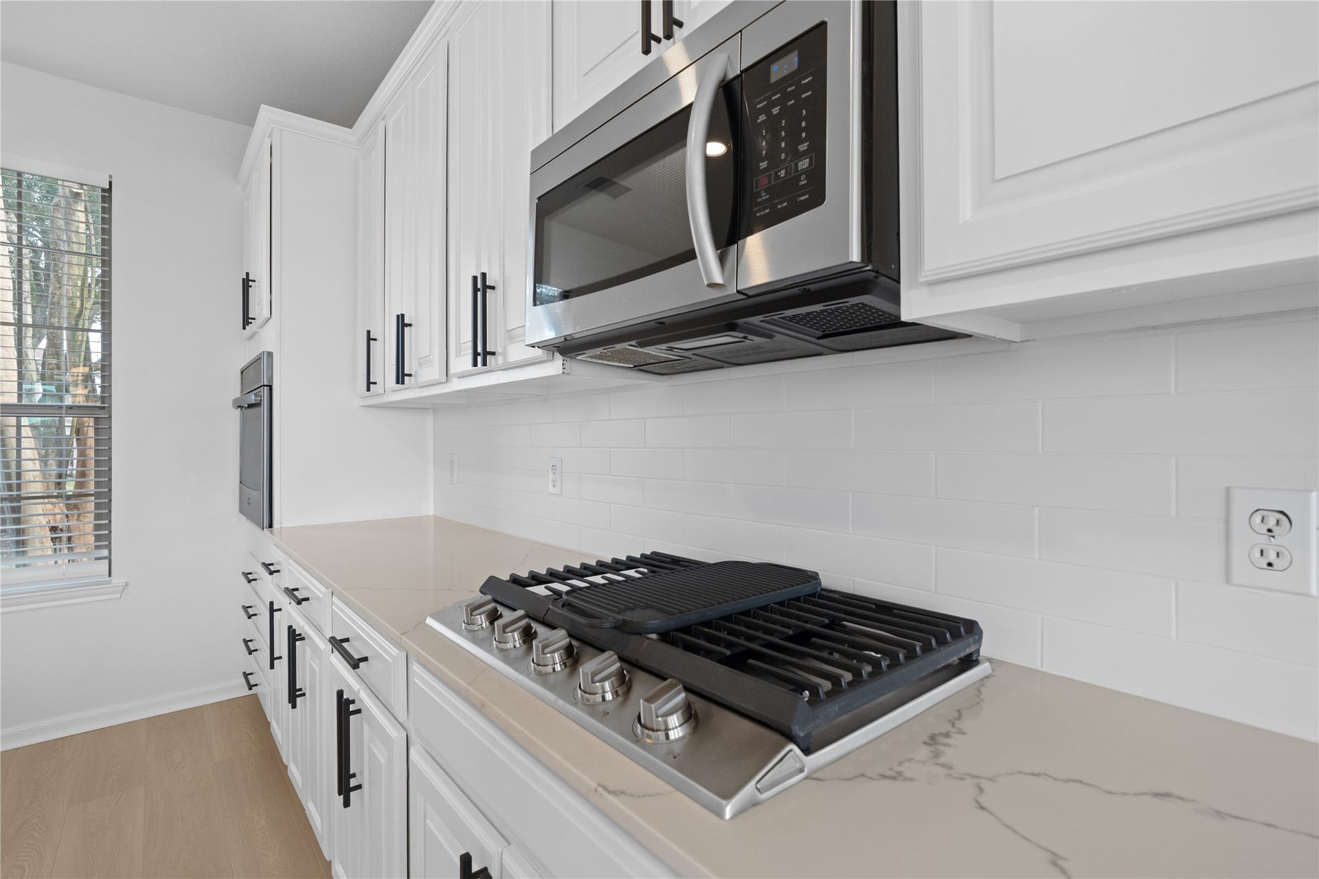 21611 Manitou Falls Lane, Katy, TX 77449 Kitchen Cooktop Close-up highlights the gas cooktop, stainless steel microwave, white subway-style backsplash, stone-look countertop, and abundant surrounding cabinetry.
