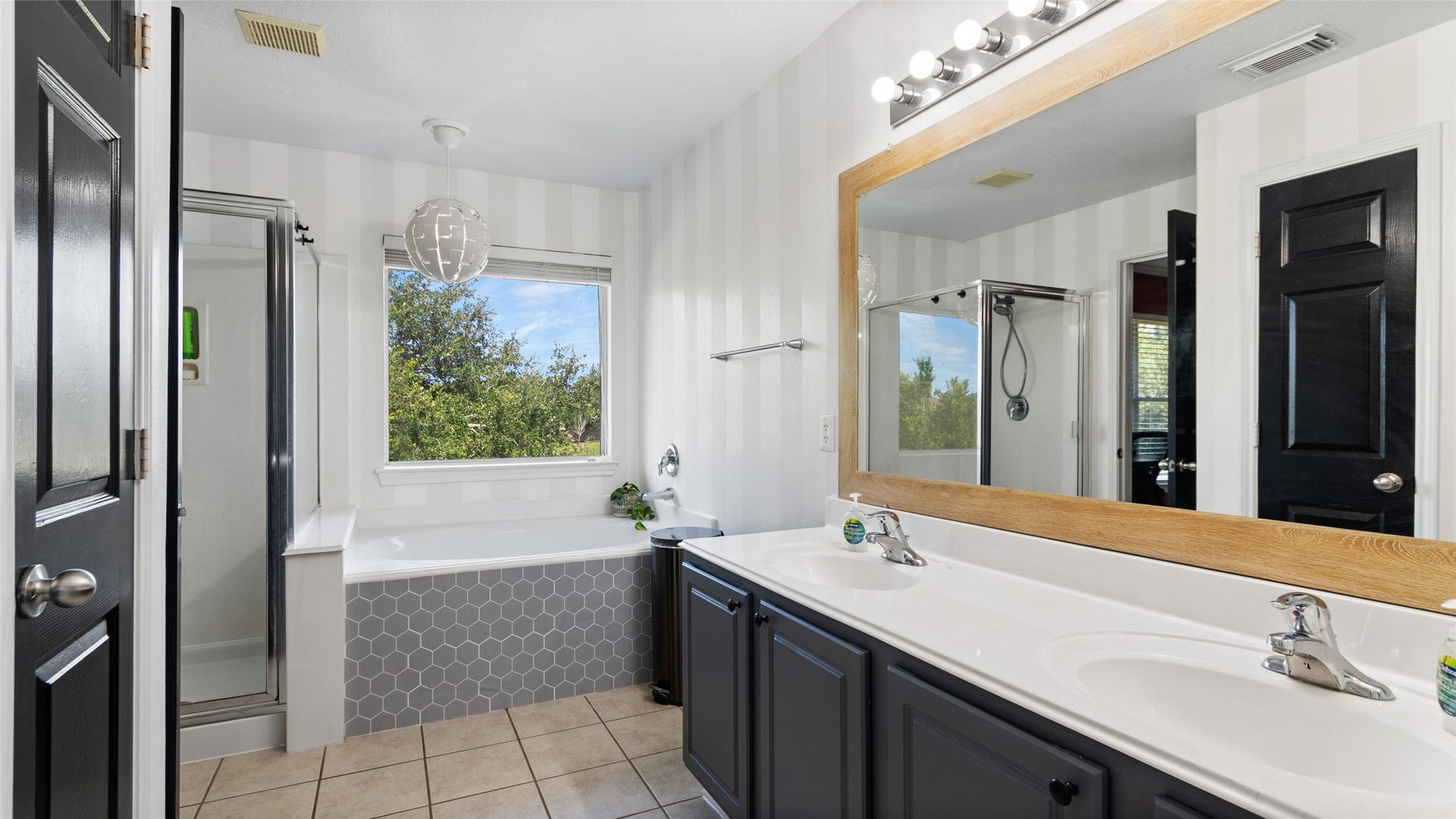 Bright bathroom featuring a large window, soaking tub, modern vanity with ample lighting, and sleek tile flooring. 417 Folk Crest Ln Dickinson, TX
