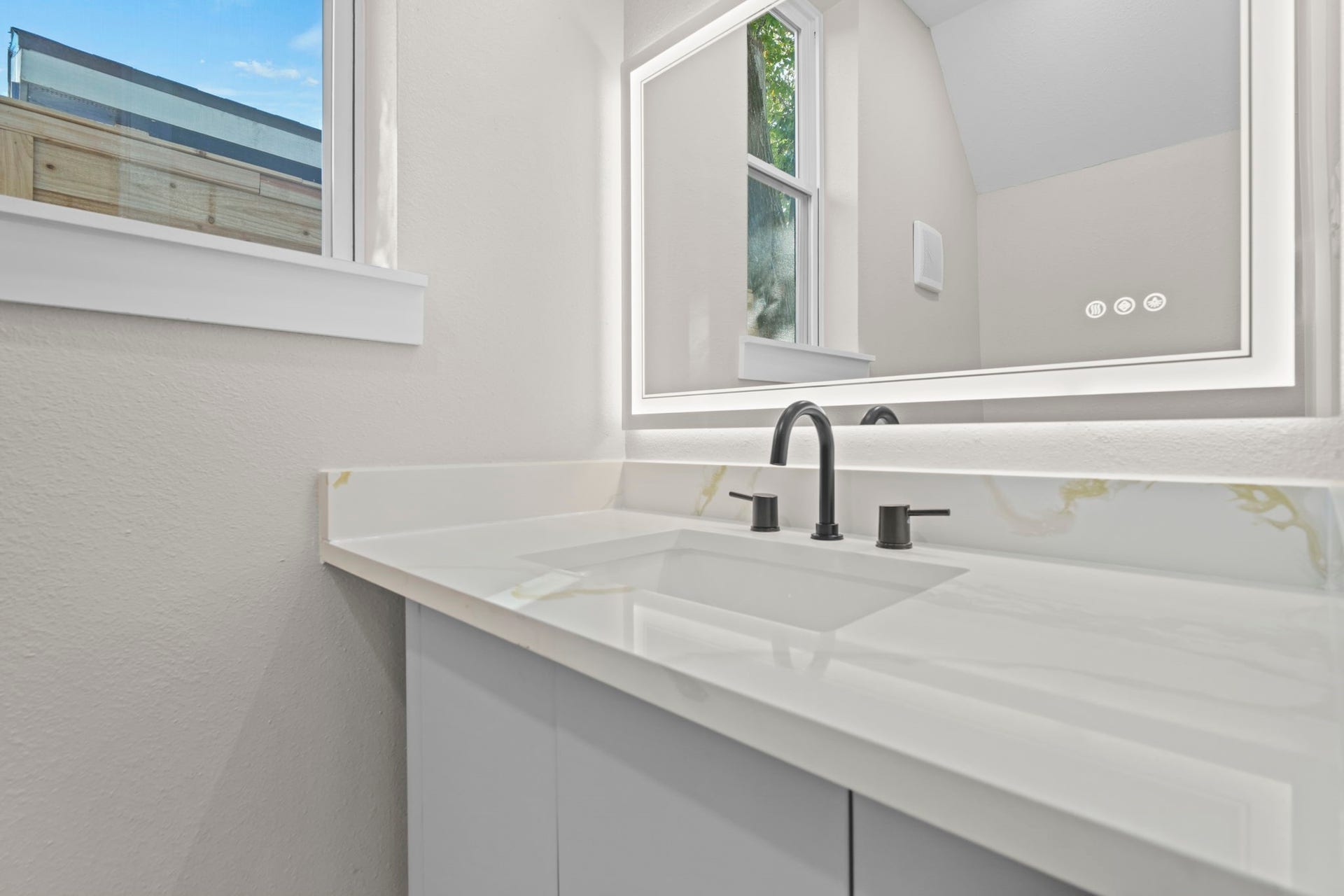 This stylish half bath features a modern floating-style vanity paired with a wide marble-patterned countertop and sleek black plumbing hardware.