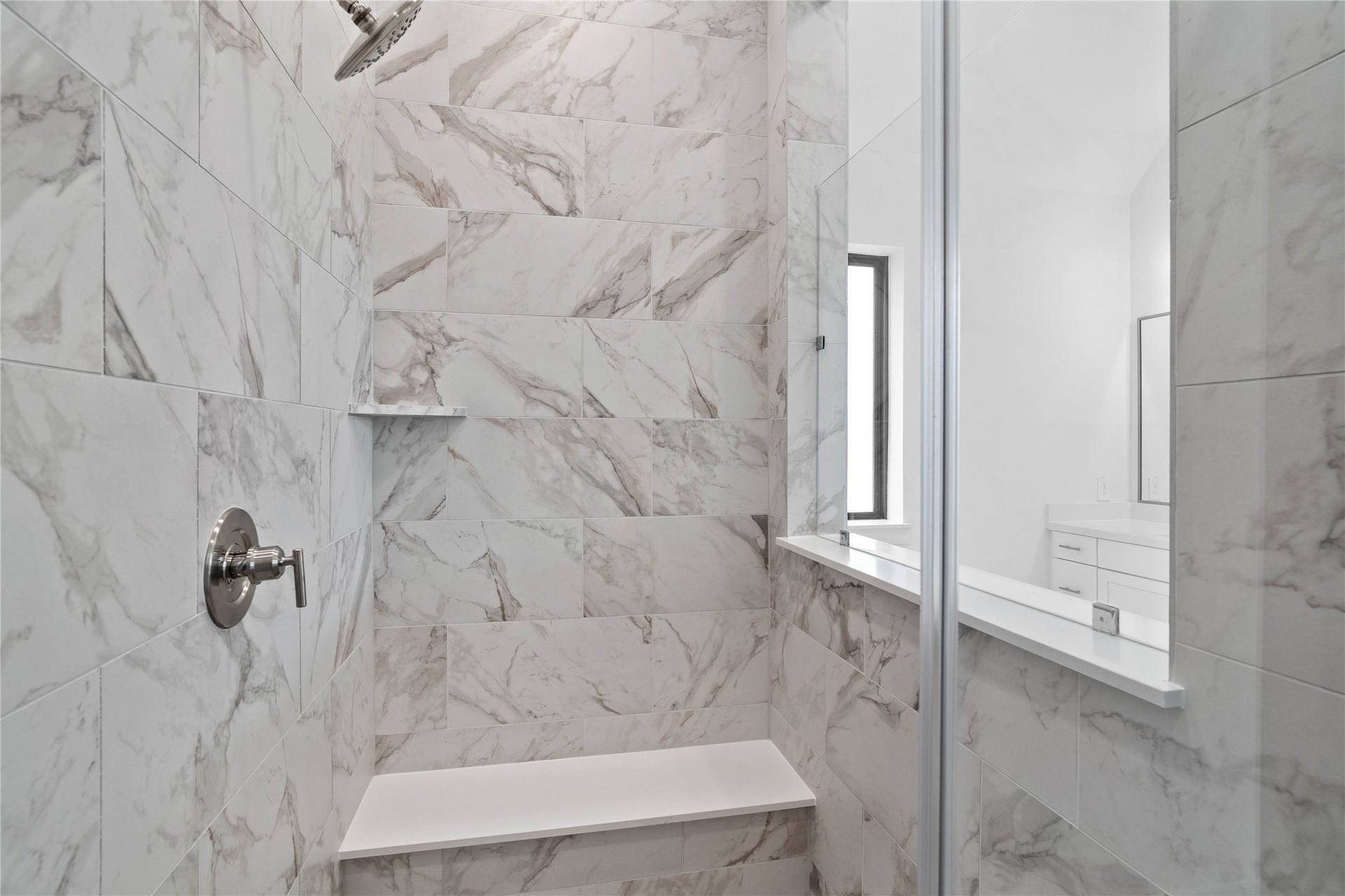 The walk-in shower includes a convenient, integrated bench with a niche shelf, offering comfort, extra storage space, and a high-end, custom appearance.