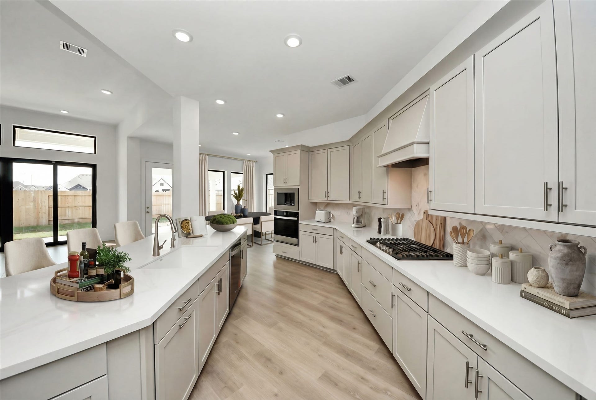 This modern kitchen features a clean, open-concept design characterized by sleek, light-toned shaker-style cabinetry and luxurious quartz countertops. The layout is centered around a spacious island that includes an undermount sink and faucet, providing both functional workspace and a gathering area.