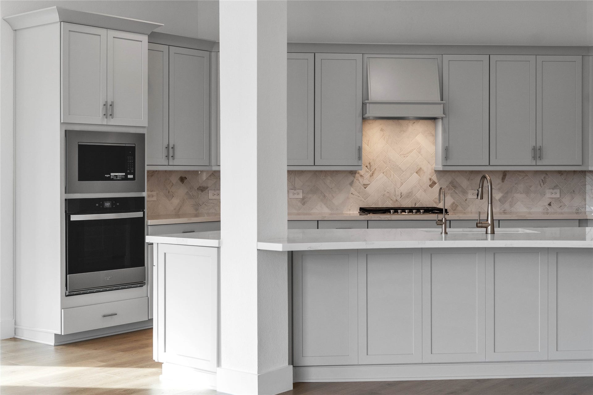 The stunning herringbone tile backsplash serves as a sophisticated focal point, featuring subtle marble-like veining that adds texture and visual depth to the space.