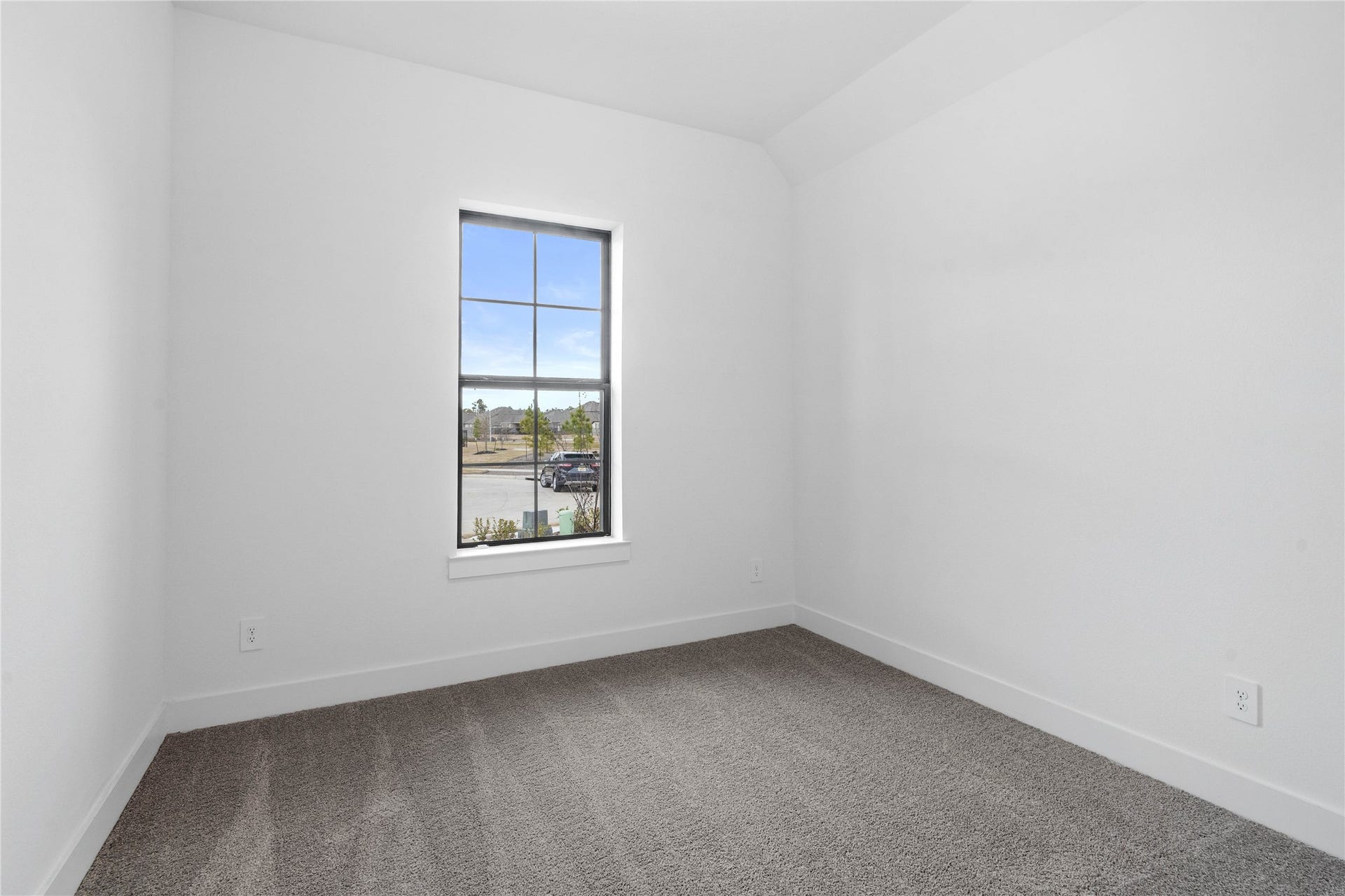 Tucked peacefully in the front of the home is this secondary bedroom featuring neutral toned walls, sloped ceiling, large window, plush carpet flooring, and a walk-in closet.