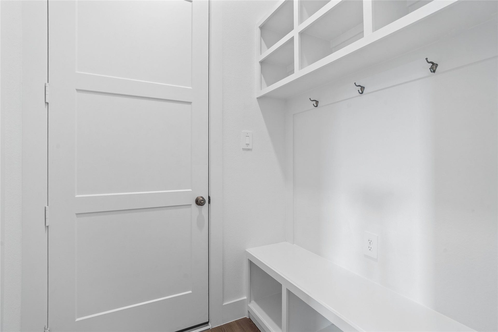 Step into this highly functional and stylish mudroom drop zone, an essential feature for a busy household. The space boasts custom-built white cabinetry and shelving, providing generous storage for coats, bags, and shoes. A comfortable built-in bench offers a convenient spot to sit, while three sleek hooks keep outerwear tidy and accessible.